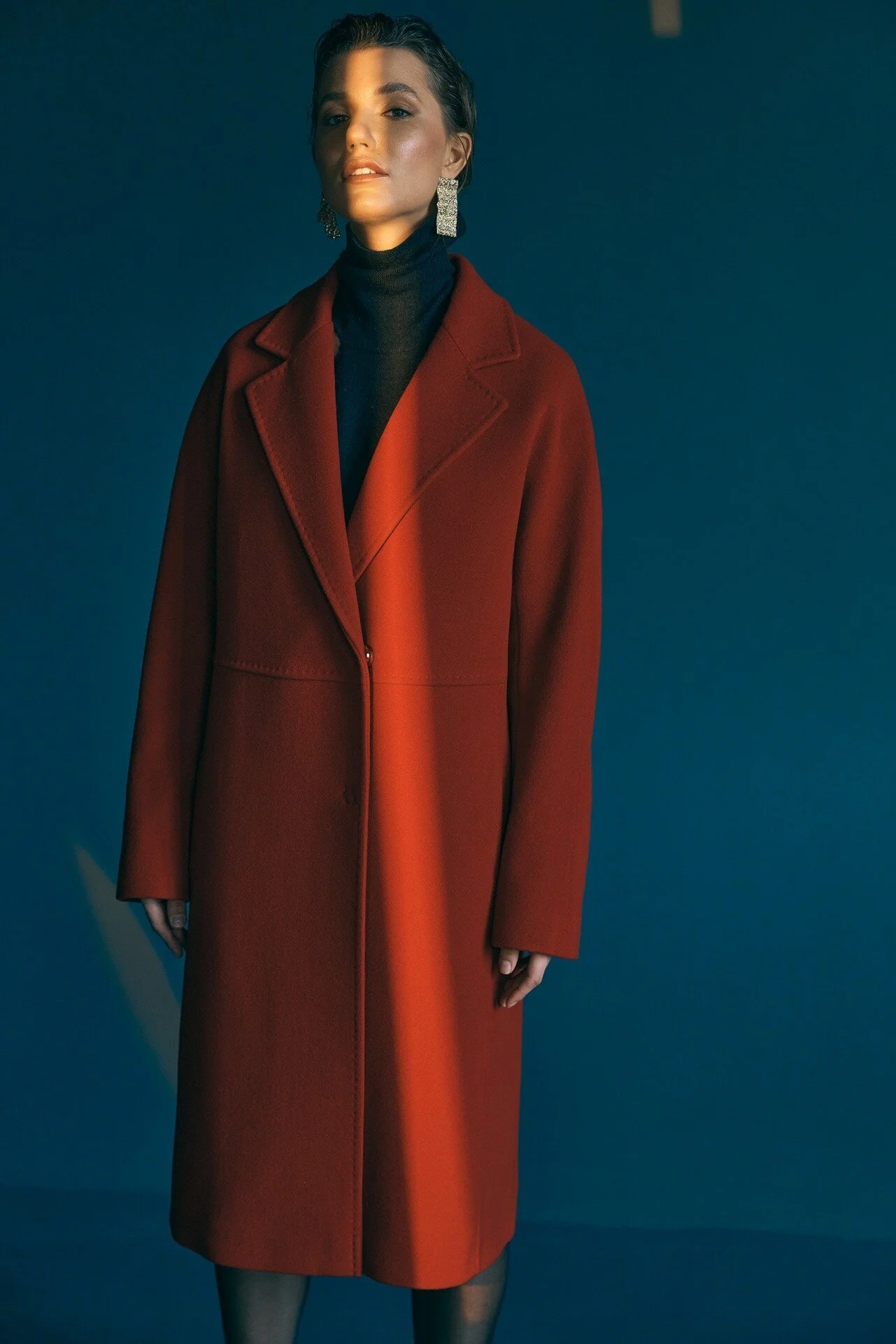 Woman_in_Red_Coat_with_Earrings_Against_Blue_Background.jpeg