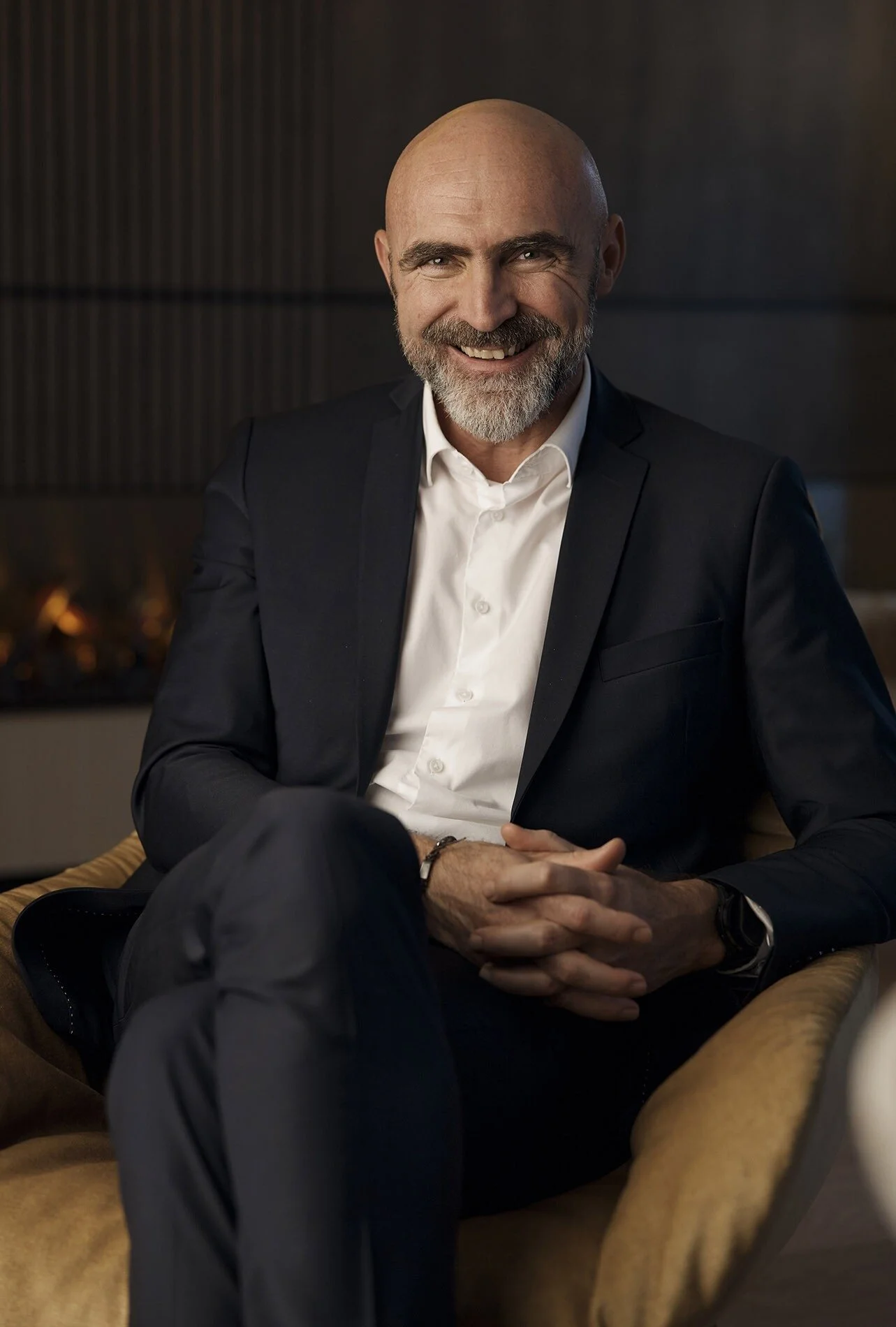 Smiling_man_in_dark_suit_seated_in_modern_interior.jpg