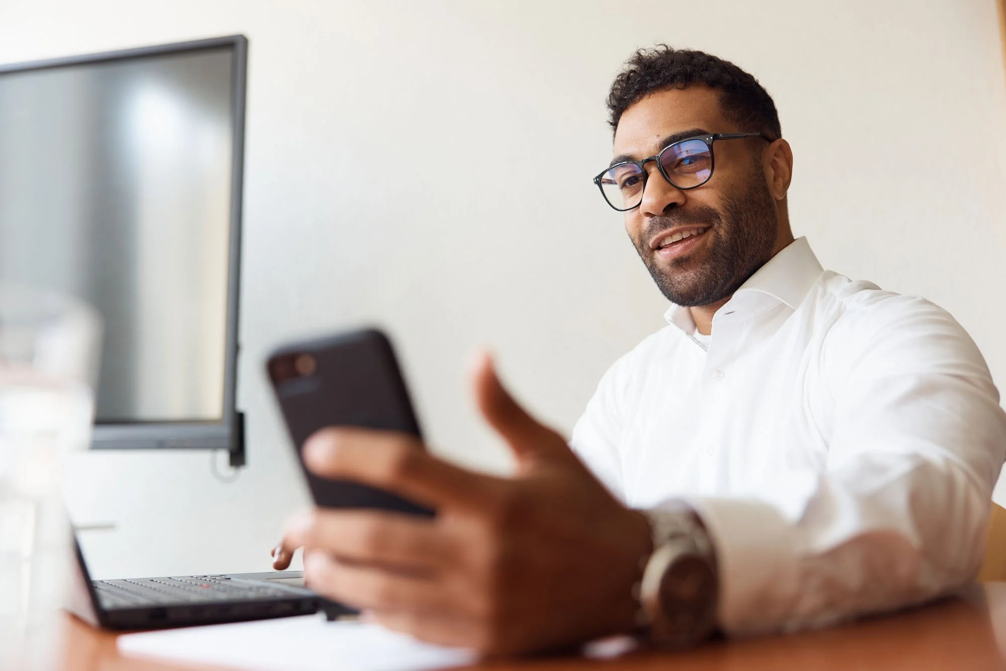 Smiling_man_in_white_shirt_using_smartphone_at_desk.jpeg