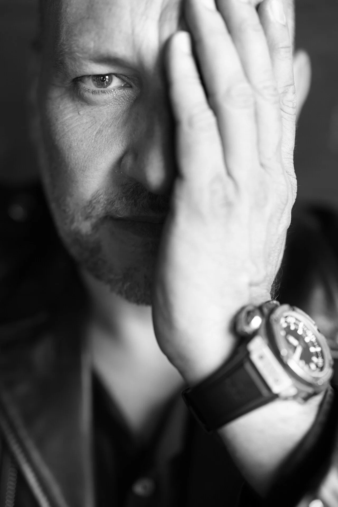 Man_in_leather_jacket_covering_half_his_face_with_hand.jpeg