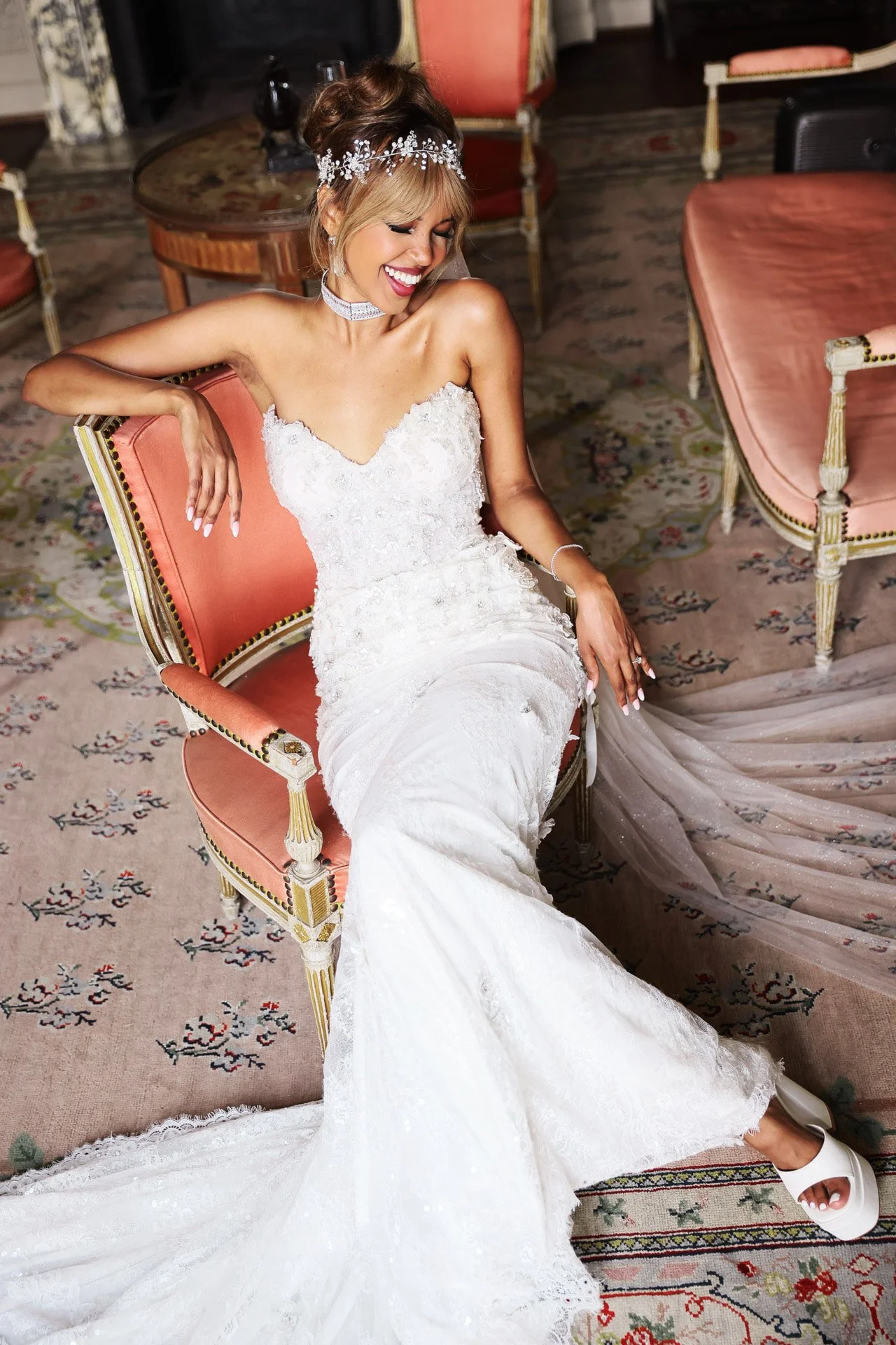 Jeune mariée en robe blanche se détendant sur une chaise rose.jpeg