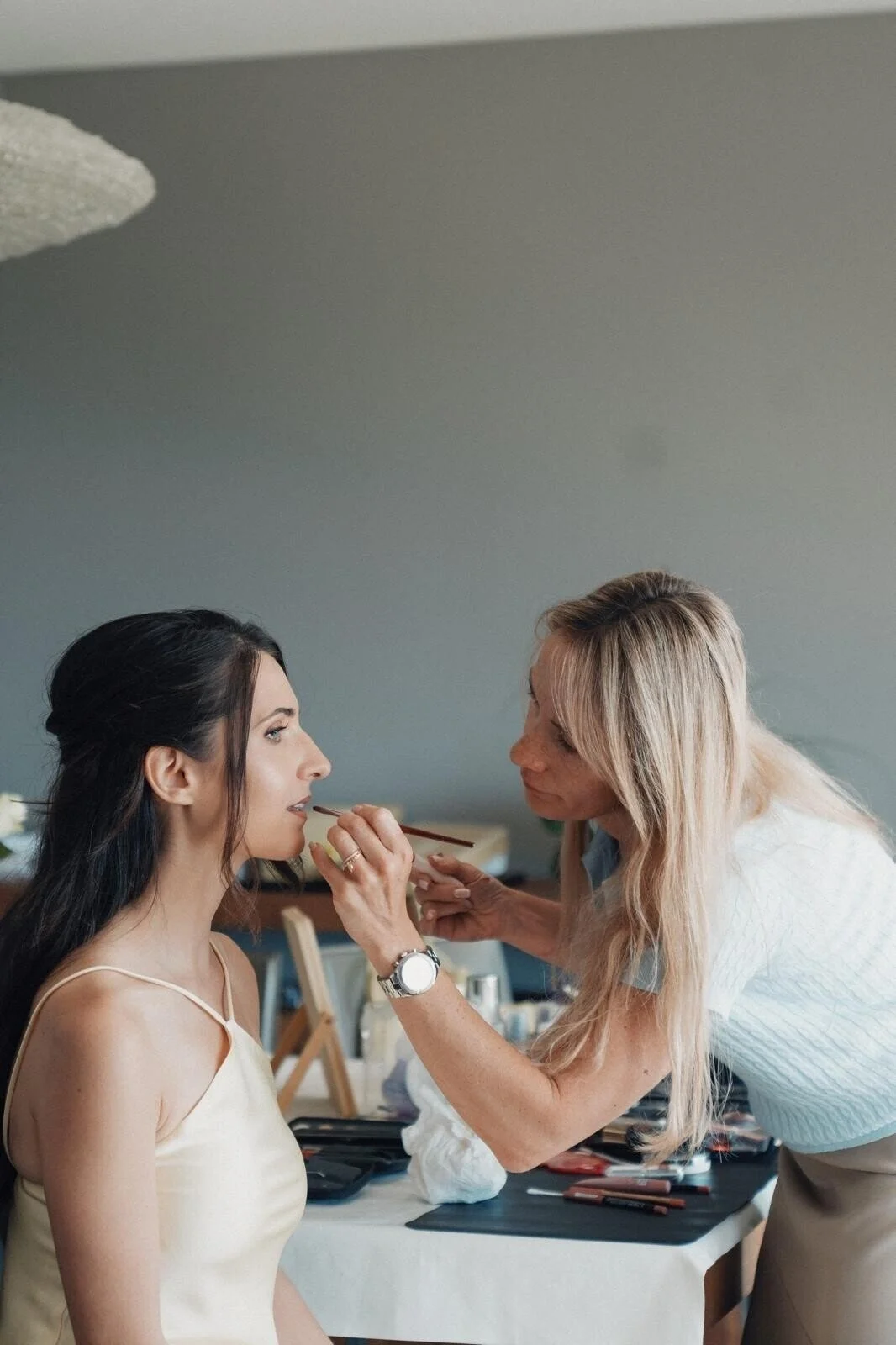 Woman_in_cream_dress_getting_makeup_applied_indoors.jpg