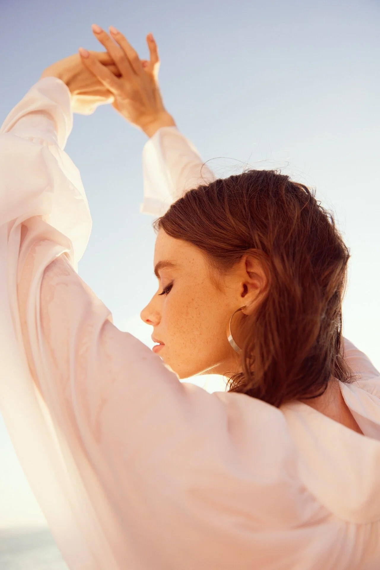 Woman_in_White_Blouse_with_Arms_Raised_Against_Blue_Sky.jpeg