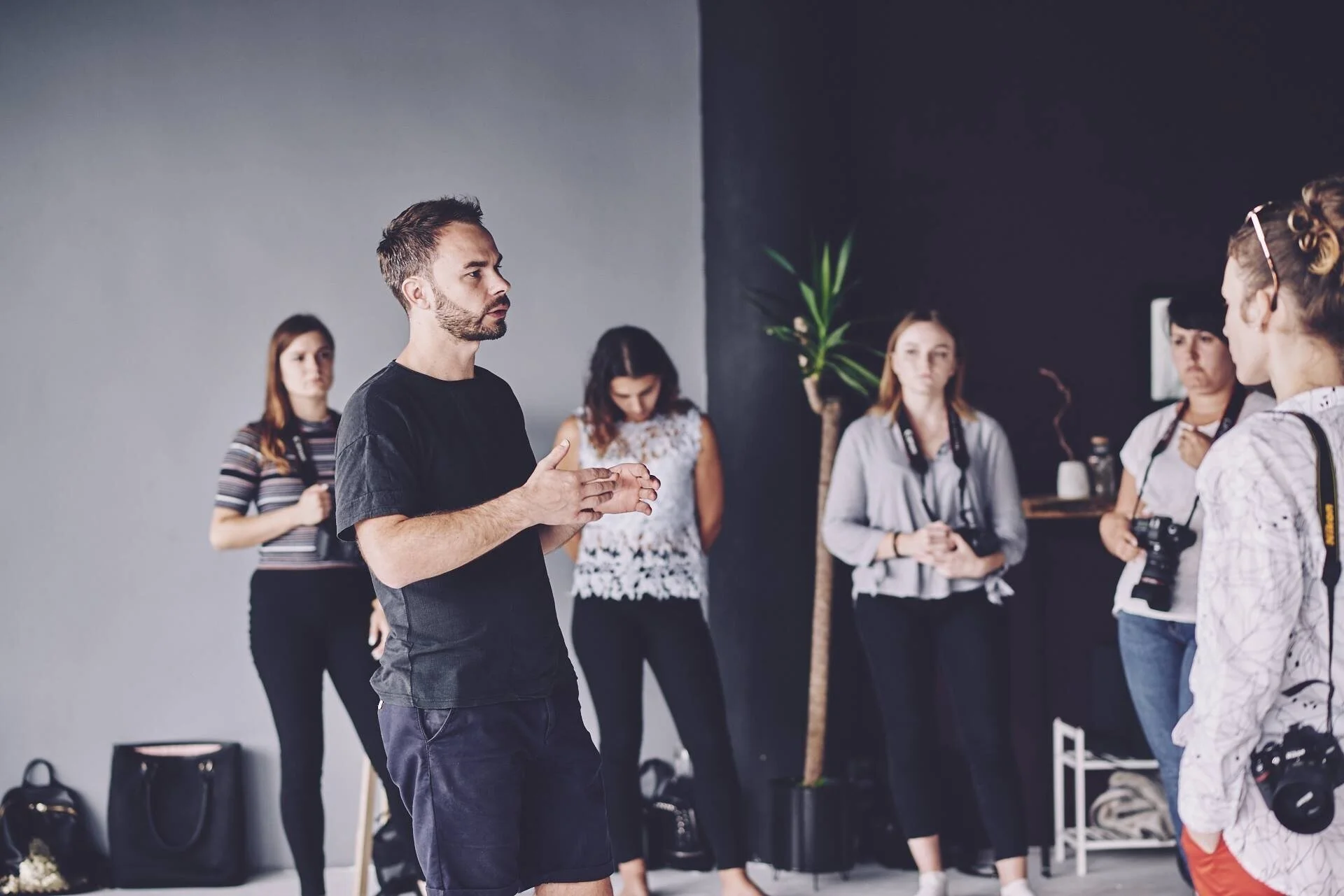 Man_Speaking_to_Group_in_Studio_with_Plants_and_Bags.jpg