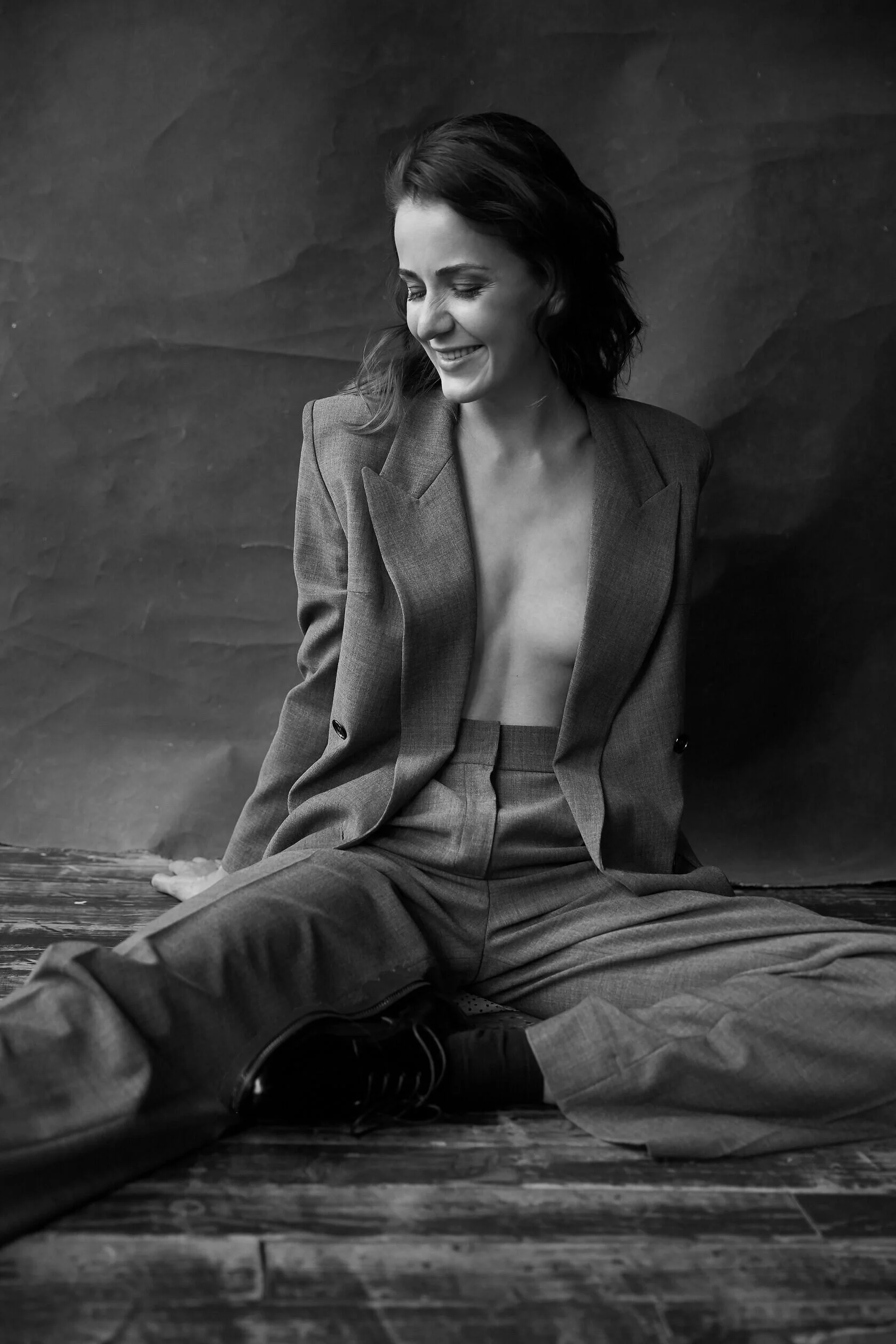 Smiling_woman_in_grey_suit_seated_on_wooden_floor.jpg
