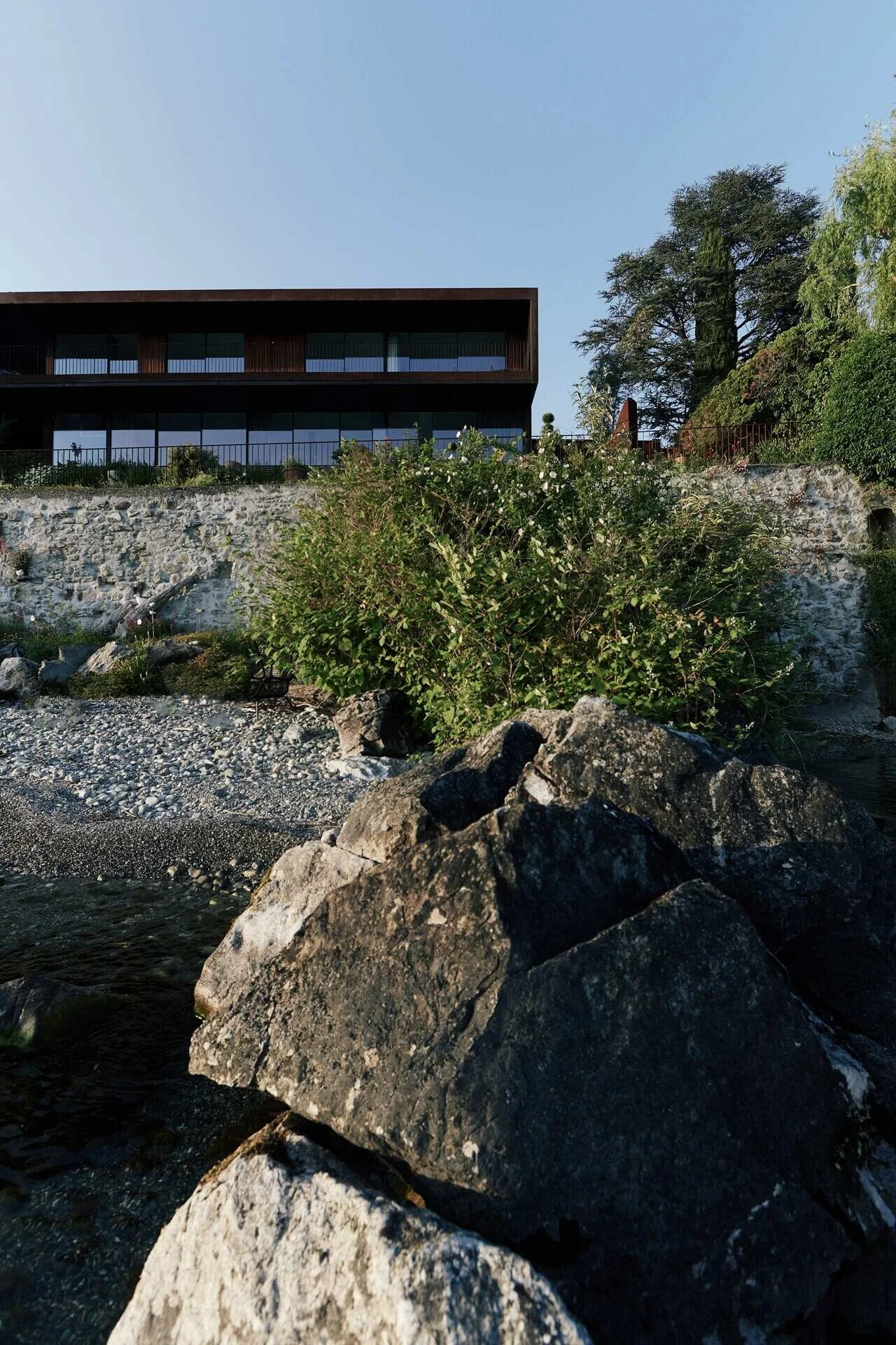 Modern_building_with_stone_wall_and_greenery_near_water.jpeg