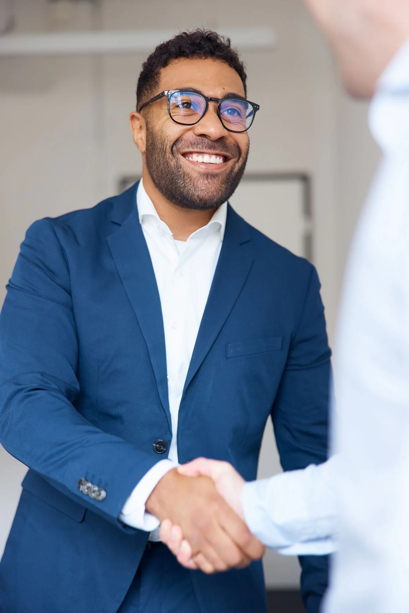 Smiling_man_in_blue_suit_shaking_hands_indoors.jpeg