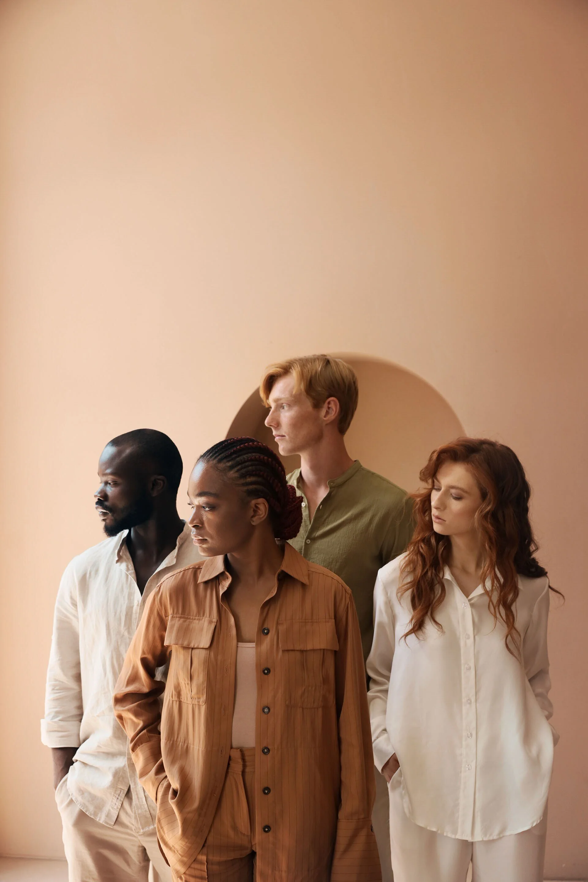 Quatre personnes se tiennent côte à côte, vêtues de vêtements aux tons neutres sur un mur rose tendre. Cette photo a été prise à Zurich par un photographe portraitiste professionnel.