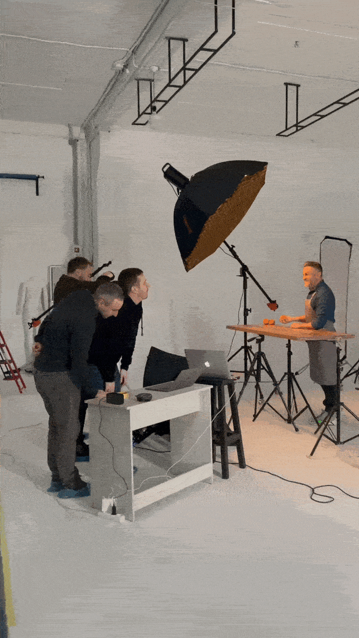 Un modèle masculin en tablier pose avec une tasse et une orange sur une table en bois. Cette photo a été prise en Suisse par un photographe professionnel.