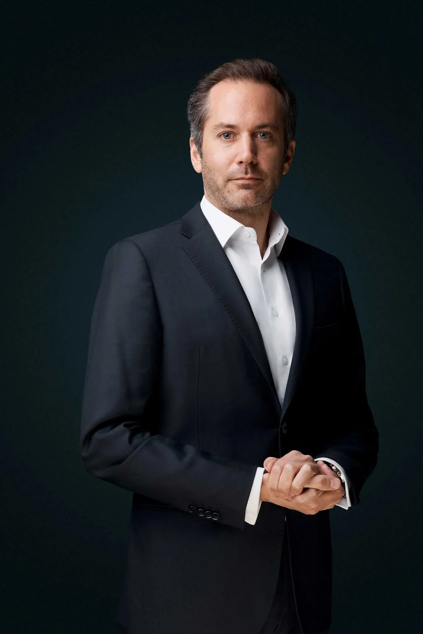 Man_in_black_suit_with_white_shirt_against_dark_background.jpg