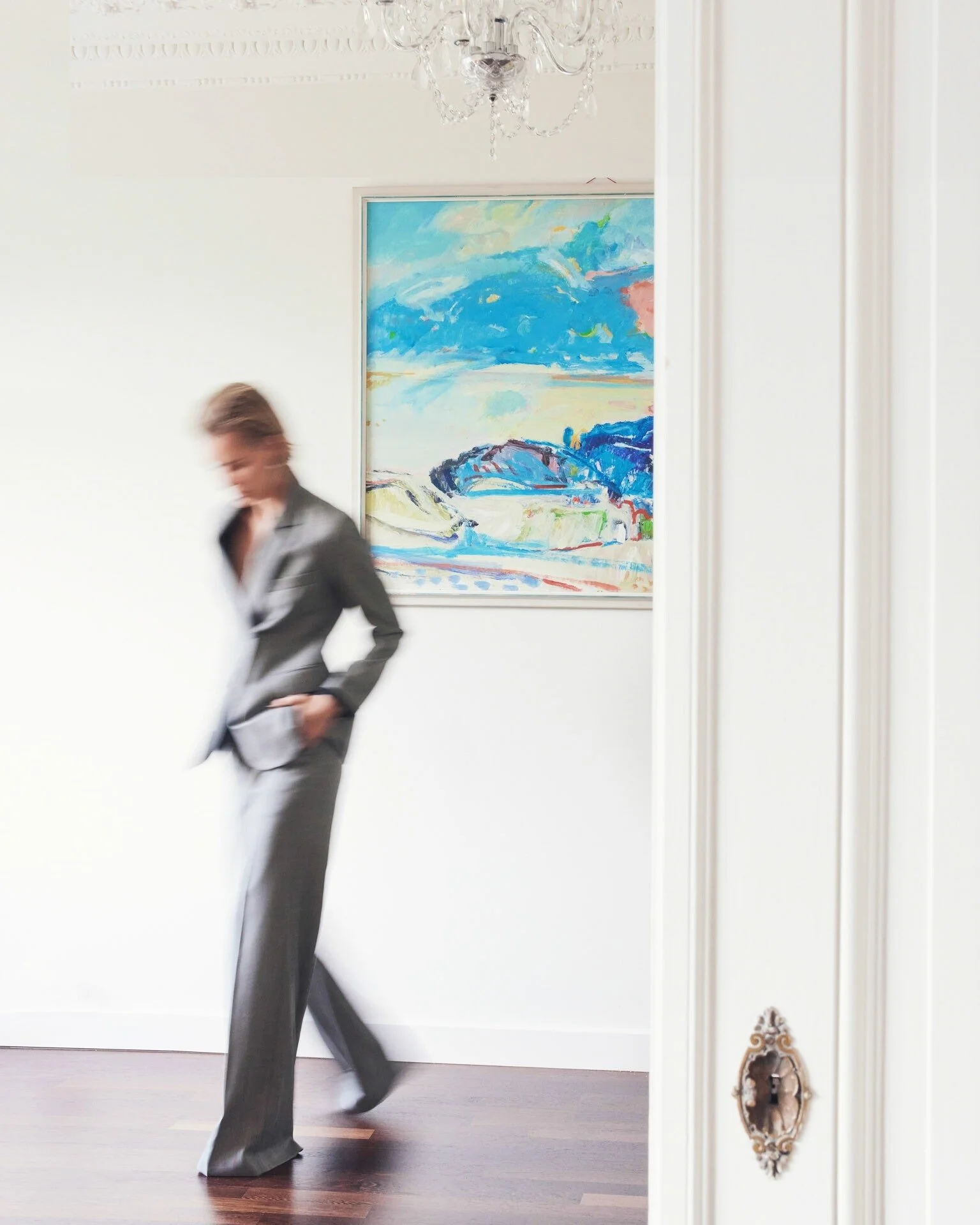 Woman_in_Grey_Suit_Walking_Past_Artwork_in_Bright_Room.jpeg
