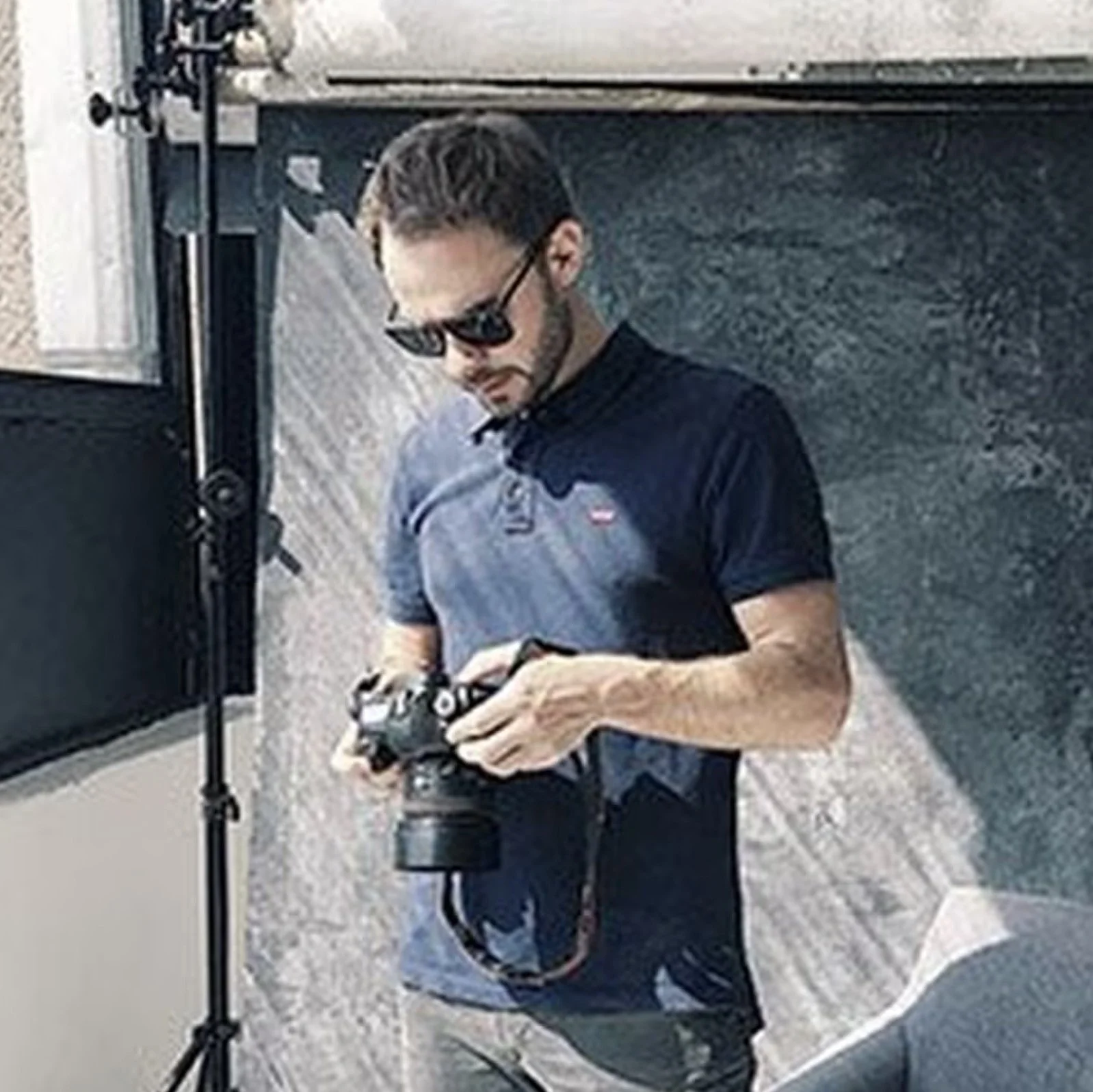 A man wearing a navy polo shirt and sunglasses is focused on his camera in a studio. Captured in Geneva by a professional portrait photographer.