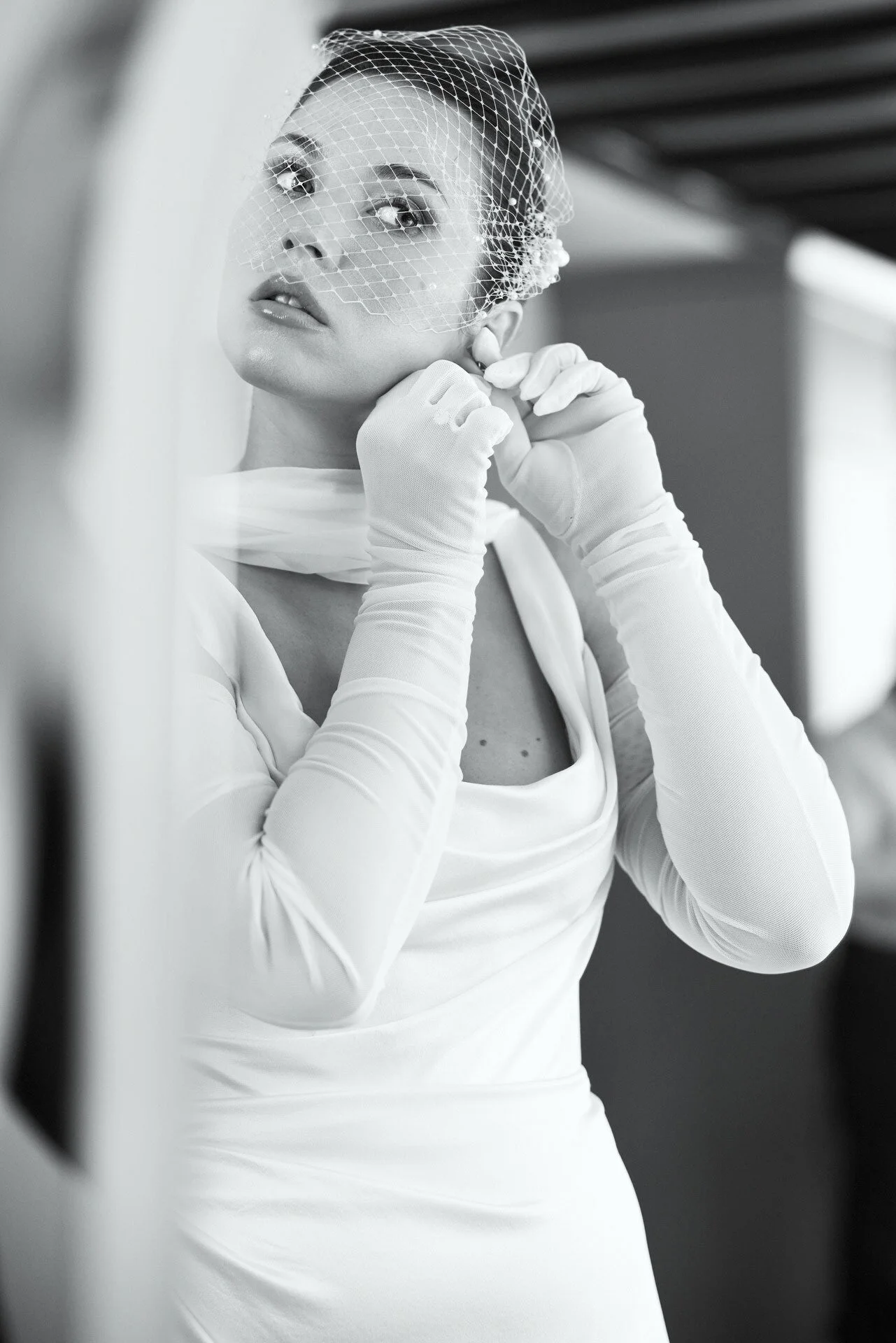 Photo en noir et blanc d'une femme en train de remettre sa boucle d'oreille en place, portant un voile et de longs gants.