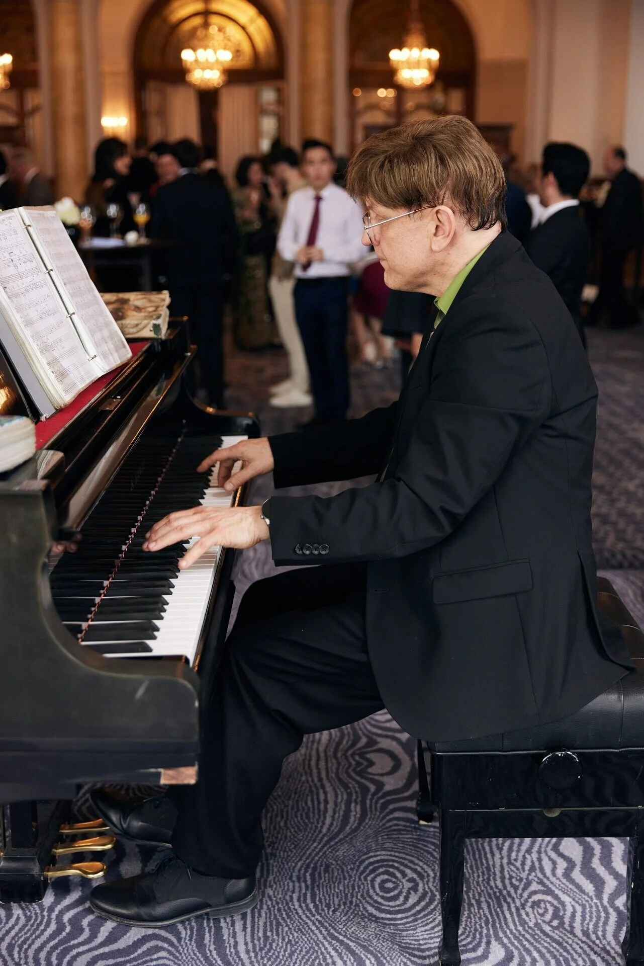Man_in_black_suit_playing_piano_with_sheet_music.jpeg