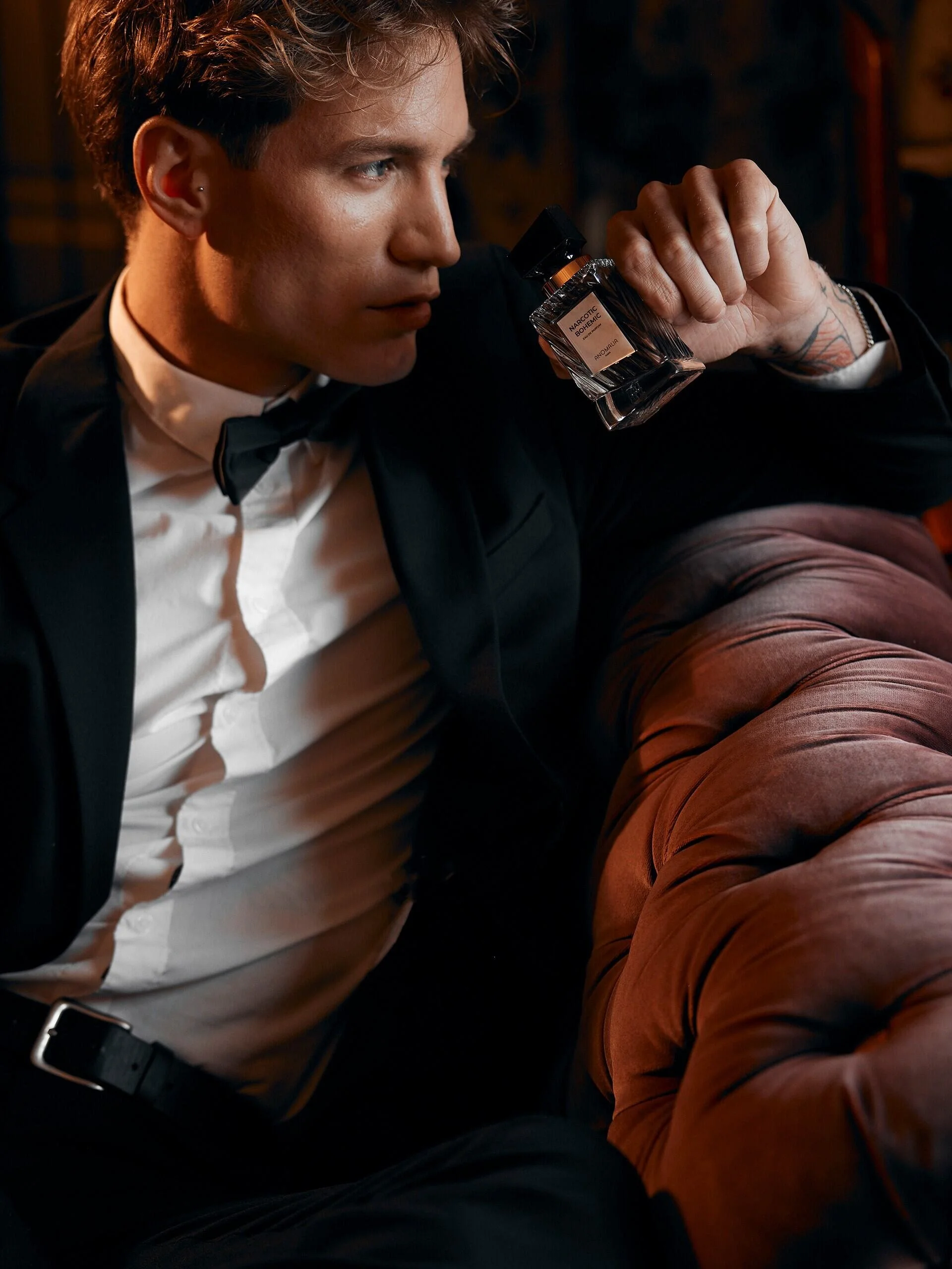 Man_in_tuxedo_holding_perfume_bottle_on_velvet_couch.jpg