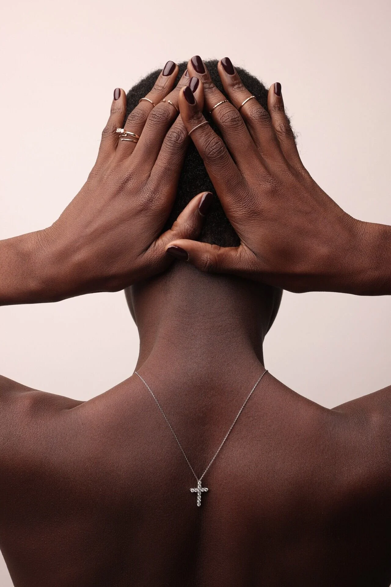 L'image représente une femme de dos, les mains sur la tête, portant un collier de croix en argent et des bagues. La photo a été prise à Zurich par un photographe professionnel.
