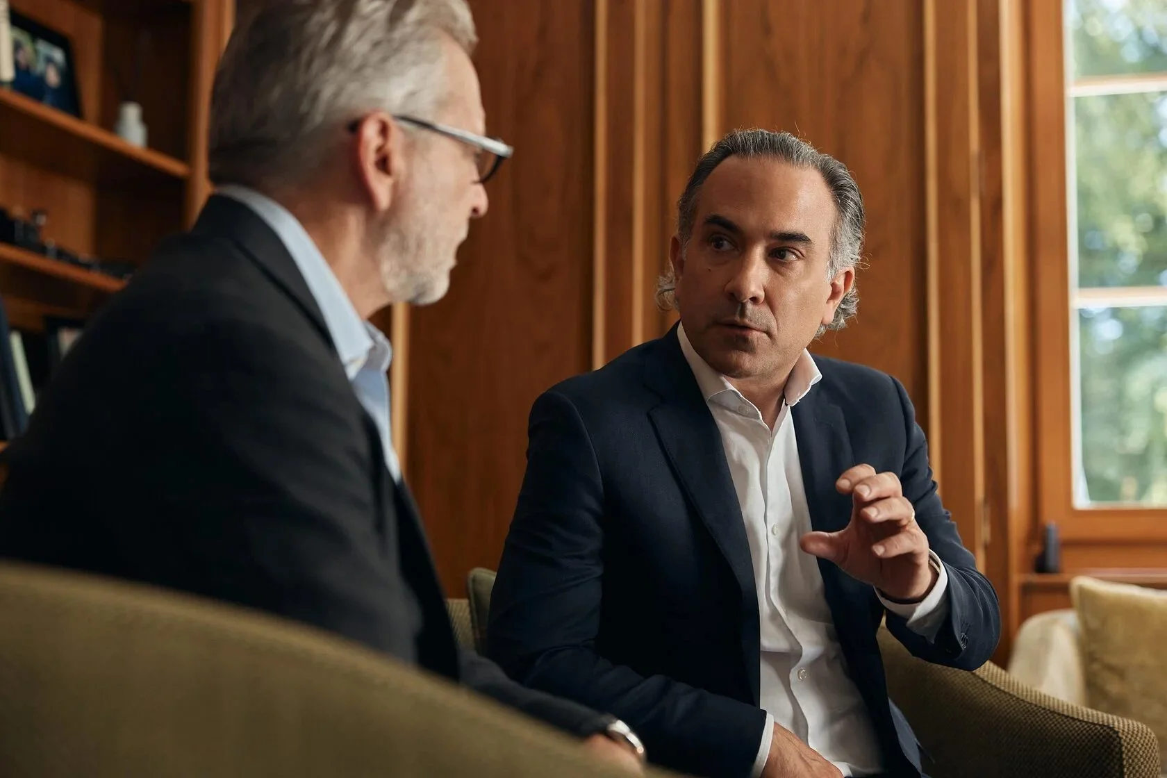 Two_men_in_suits_discussing_in_a_wooden-paneled_room.jpg