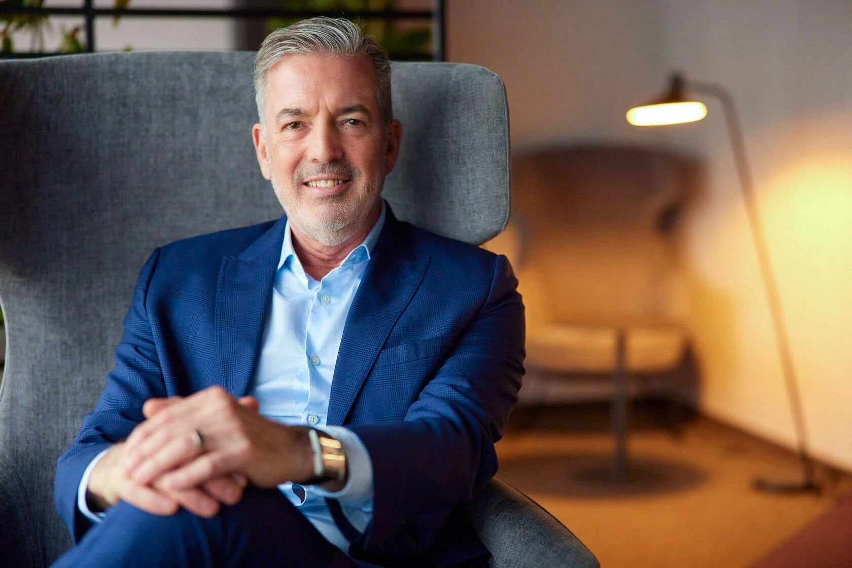 Man_in_blue_suit_sitting_in_modern_chair_with_warm_lighting.jpg
