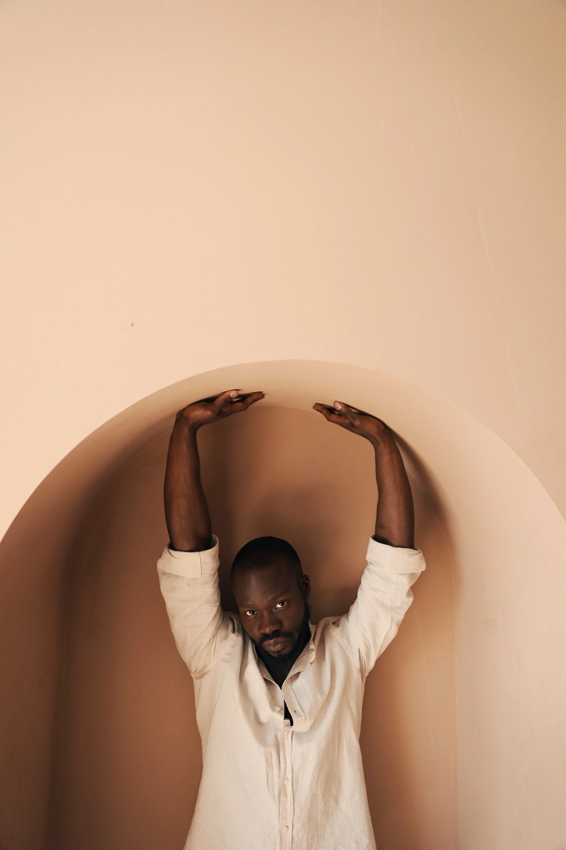Man_in_beige_shirt_posing_under_archway_with_arms_raised.jpg