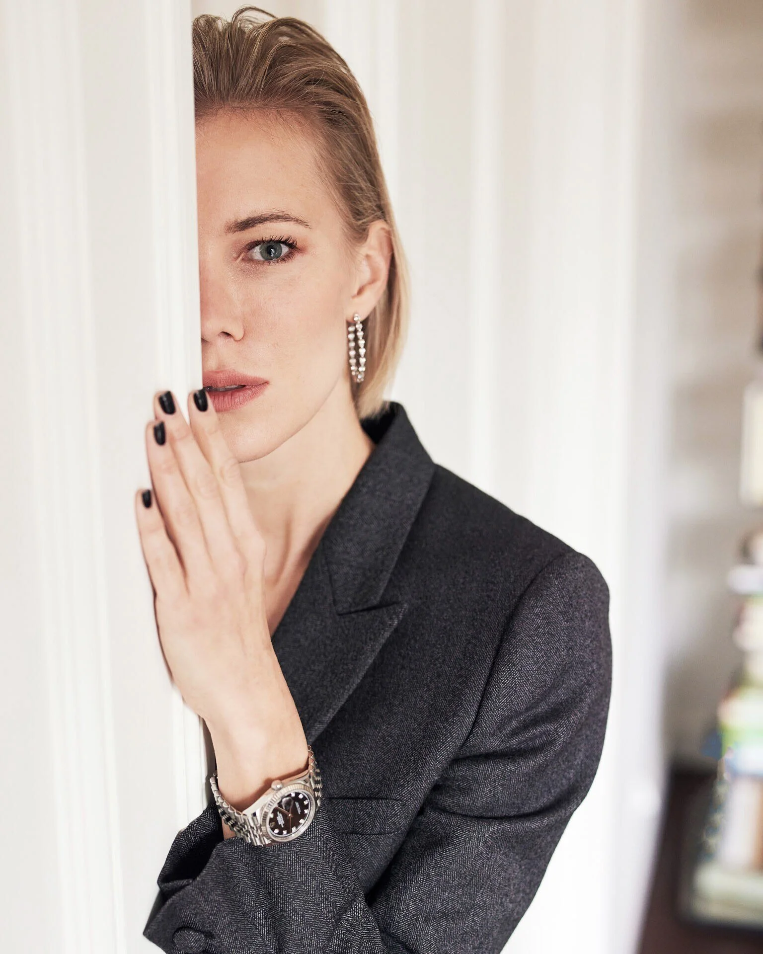 Woman_in_grey_blazer_with_watch_partially_hidden_behind_wall.jpeg