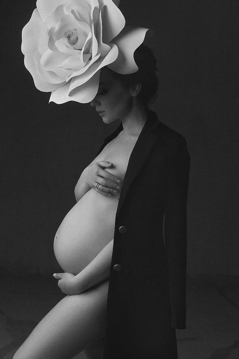 Pregnant_woman_in_black_coat_with_large_white_flower_headpiece.jpg