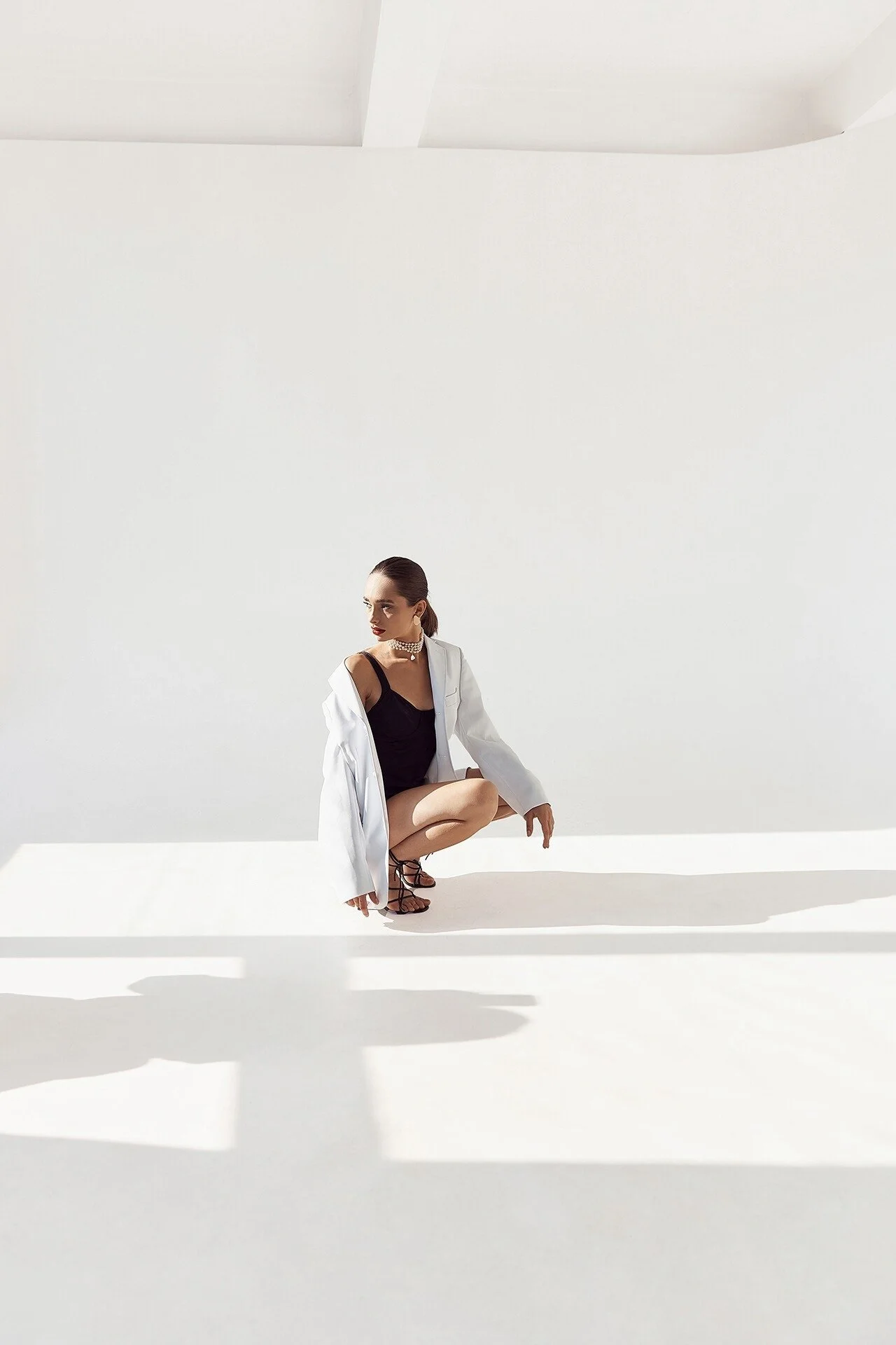 Woman_in_white_blazer_and_black_outfit_squatting_indoors.jpeg