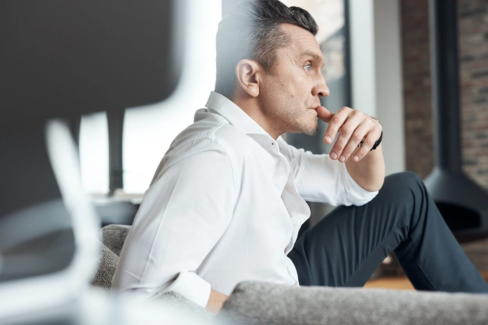 Thoughtful_man_in_white_shirt_sitting_on_a_sofa.jpeg