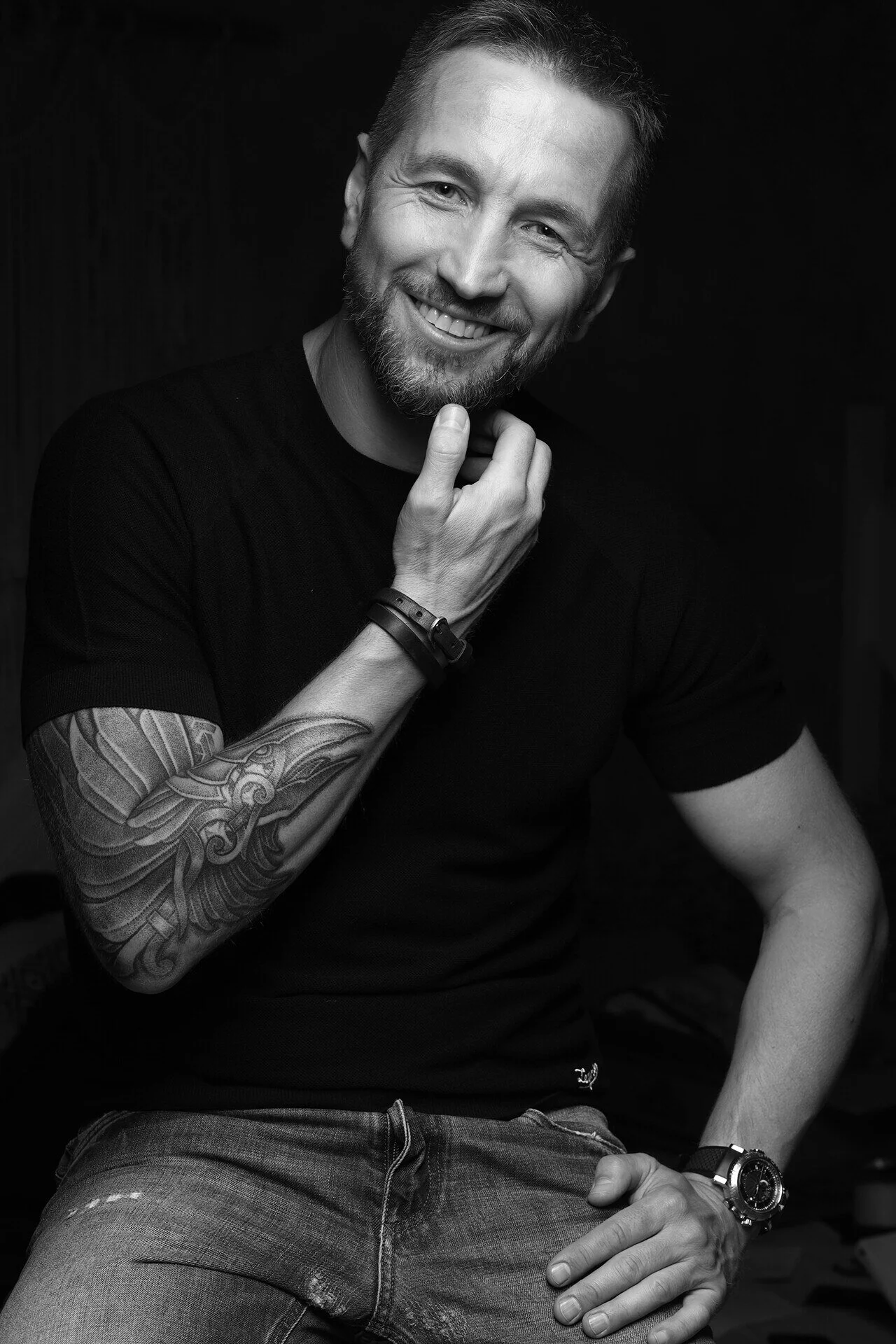 Smiling_man_in_black_shirt_with_tattooed_arm.jpg
