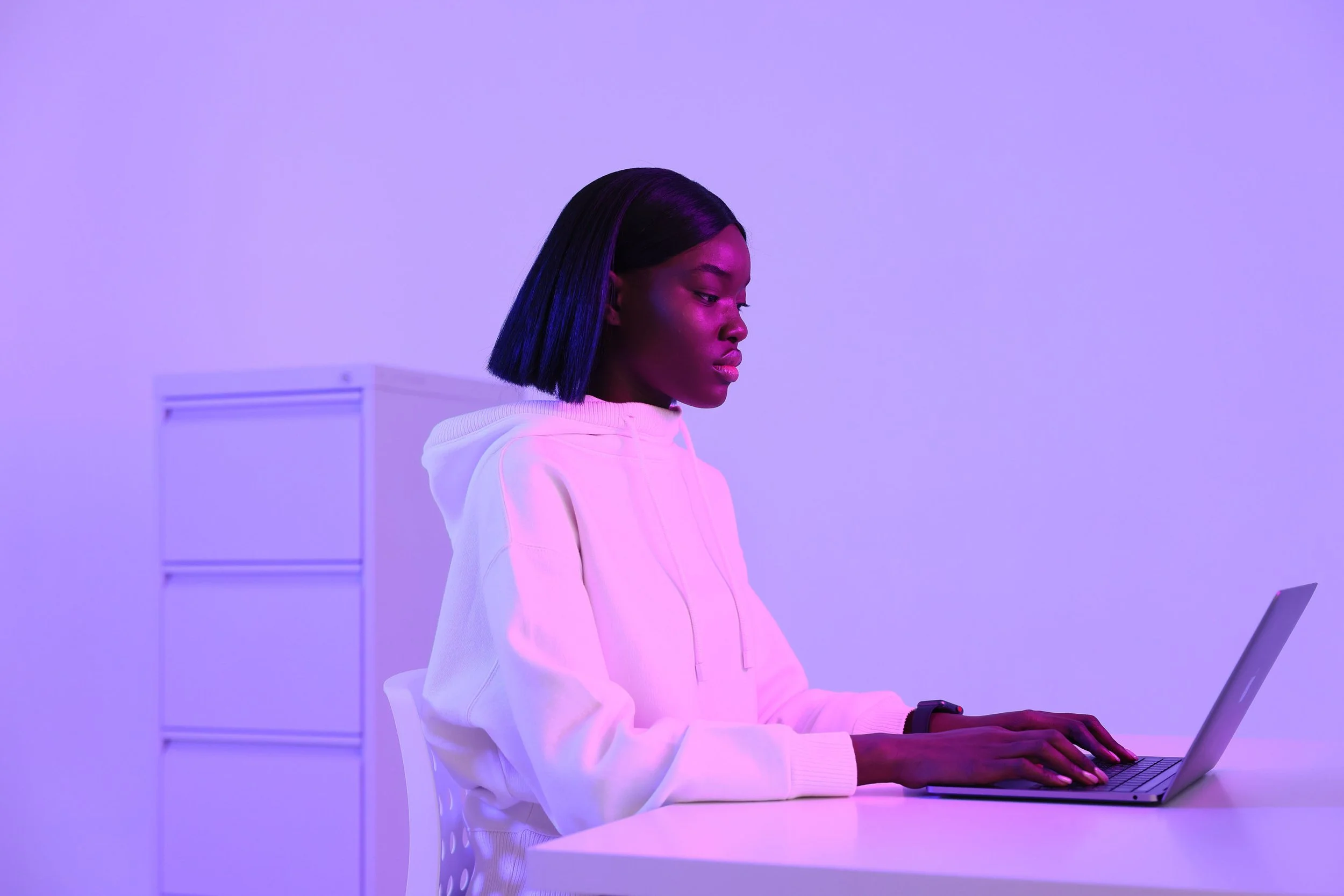 Jeune femme en cagoule blanche tapant sur un ordinateur portable avec un éclairage violet.jpg