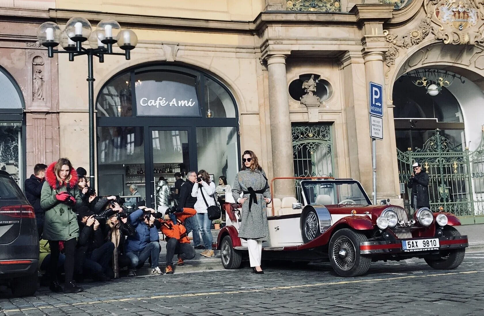 Woman_in_grey_coat_with_red_scarf_by_vintage_car_outside_caf.jpg