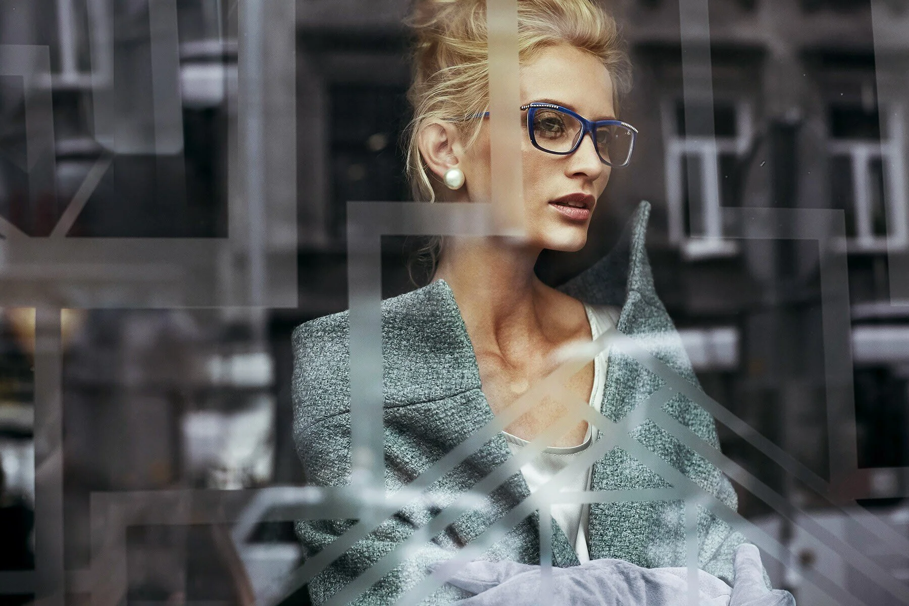 Woman_in_glasses_with_grey_coat_looking_through_window.jpg