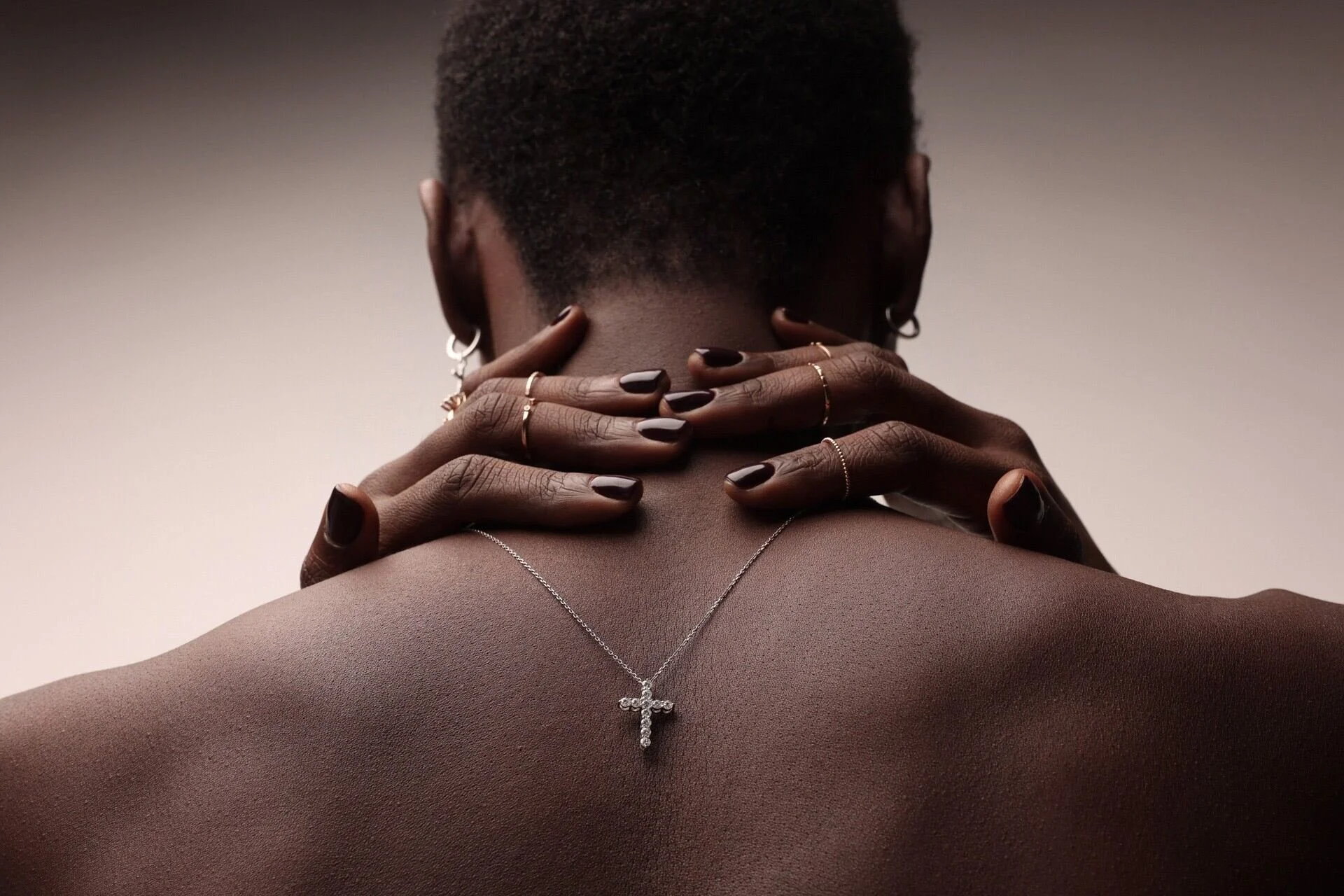 L'image montre en gros plan une épaule nue ornée d'un collier en forme de croix, sur laquelle reposent des mains au vernis à ongles sombre. La photo a été prise à Zurich par un photographe professionnel.
