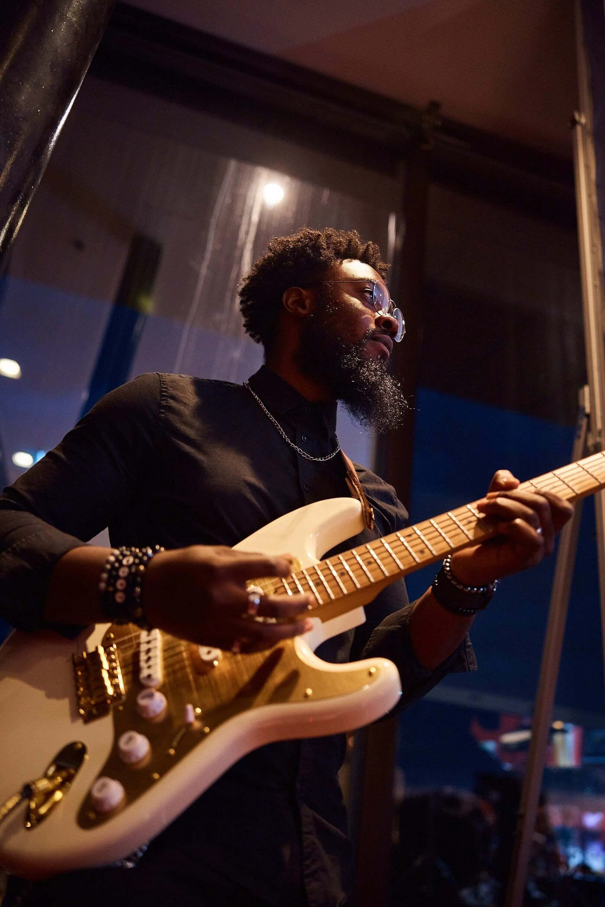 Man_playing_white_electric_guitar_in_dimly_lit_venue.jpg