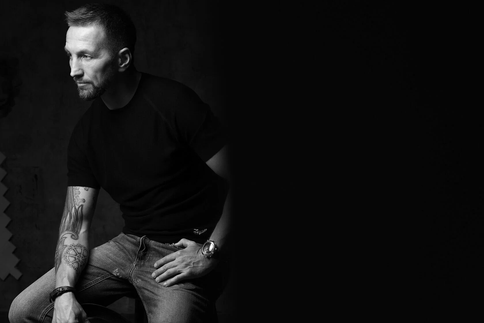 Man_in_black_shirt_and_jeans_with_tattoos_in_studio_lighting.jpg