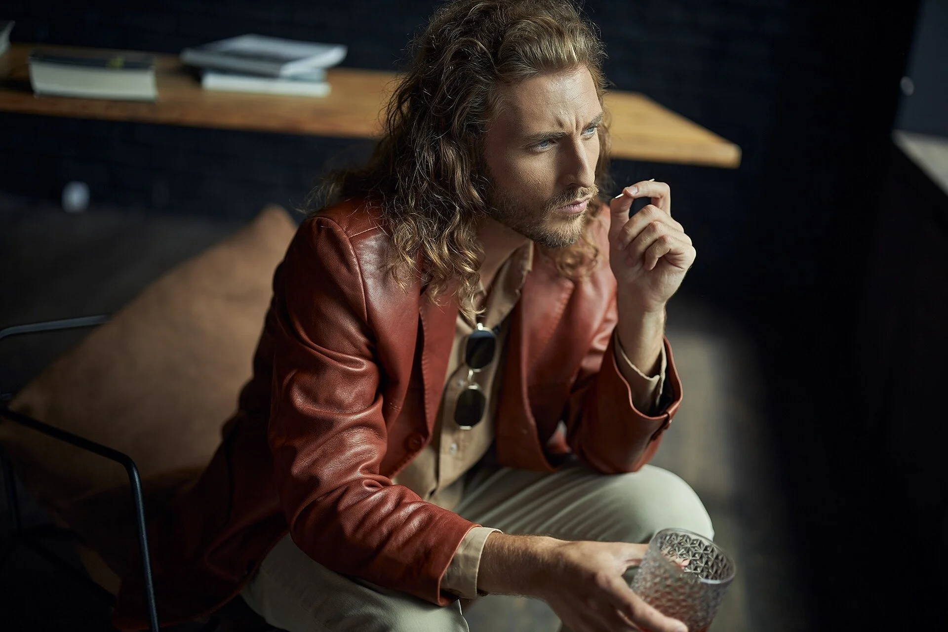 Man_in_brown_leather_jacket_holding_glass_in_modern_setting.jpeg