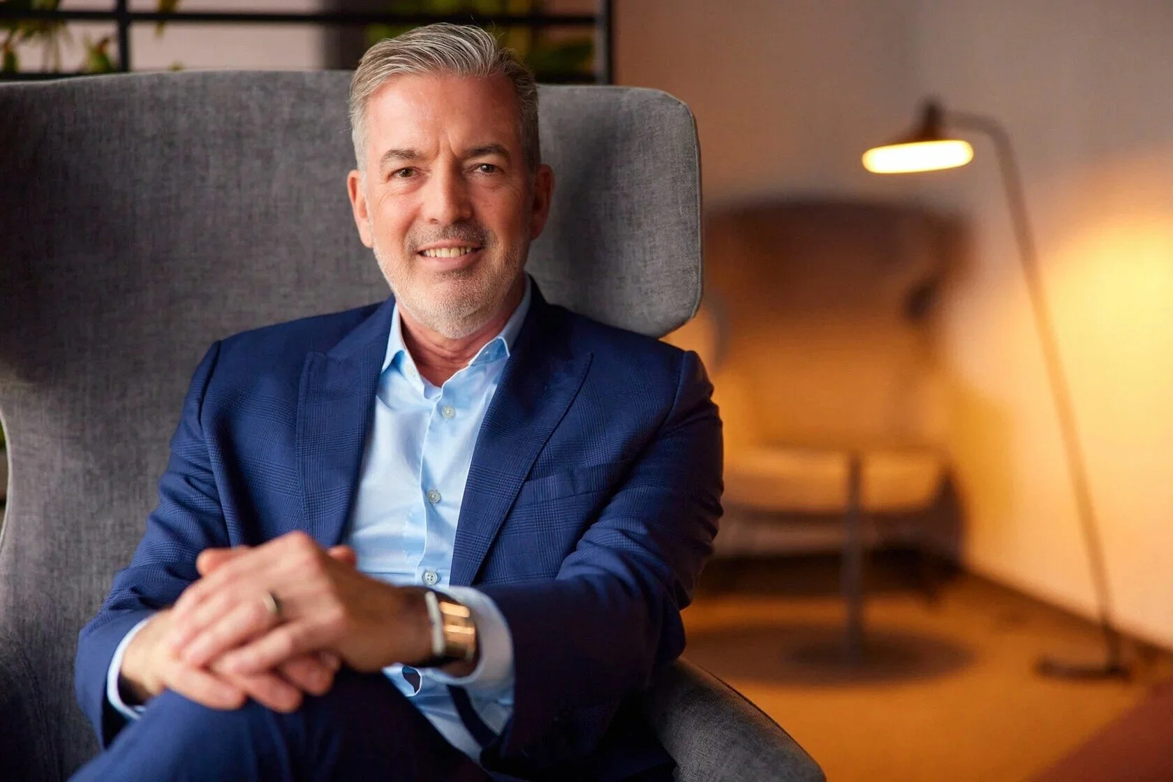 Smiling_man_in_blue_suit_seated_in_modern_armchair.jpg