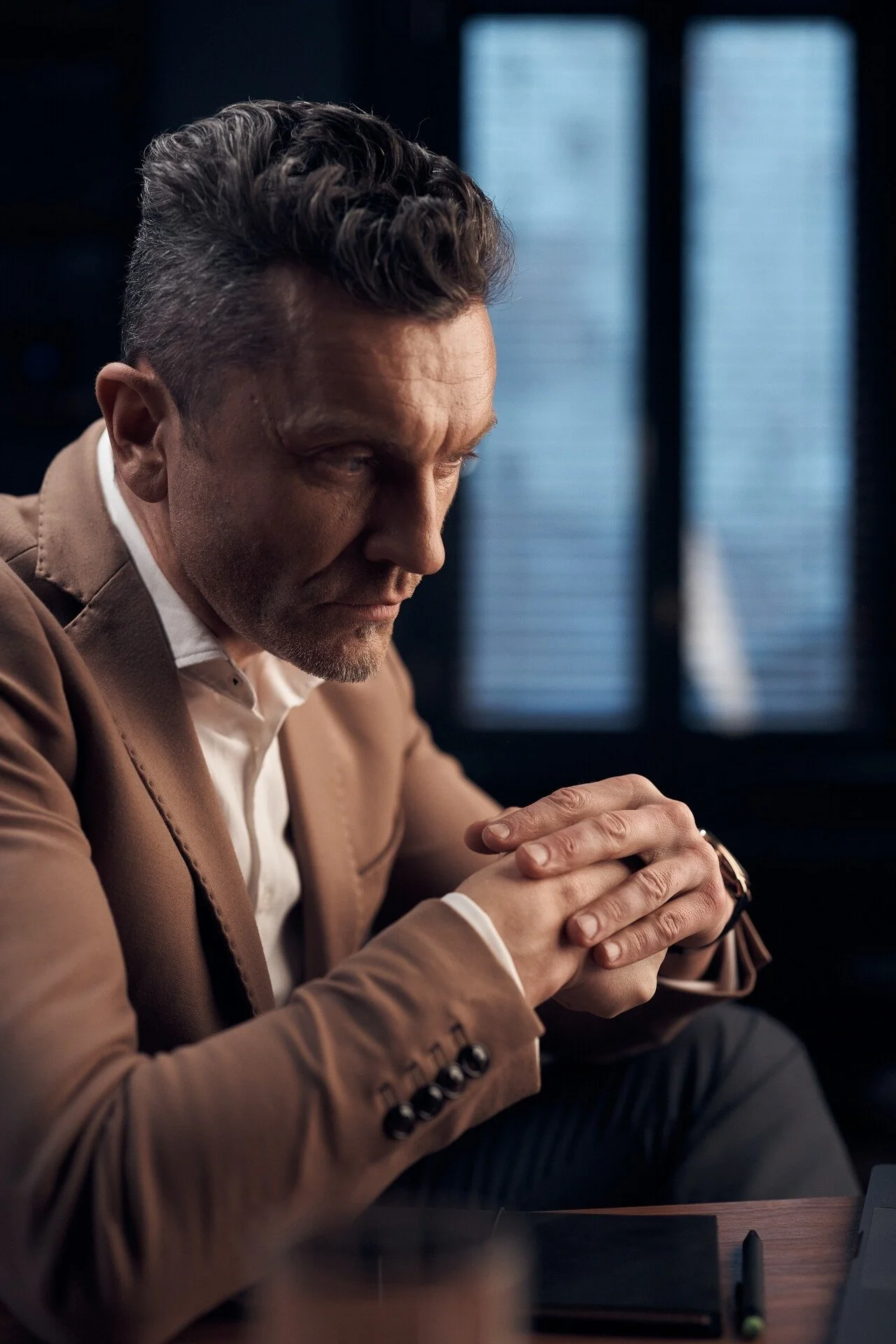 Man_in_Brown_Suit_with_Hands_Clasped_in_Thoughtful_Pose.jpeg