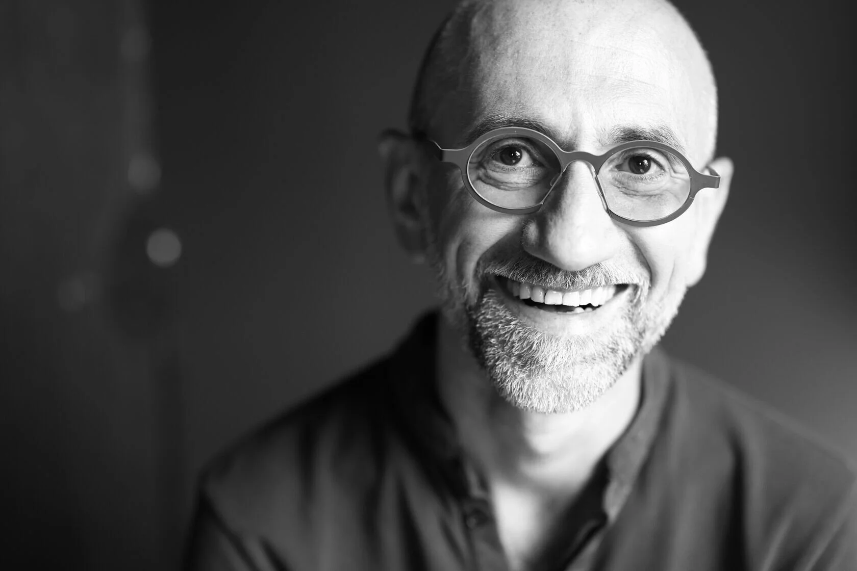 Smiling_man_with_glasses_in_dark_setting.jpeg