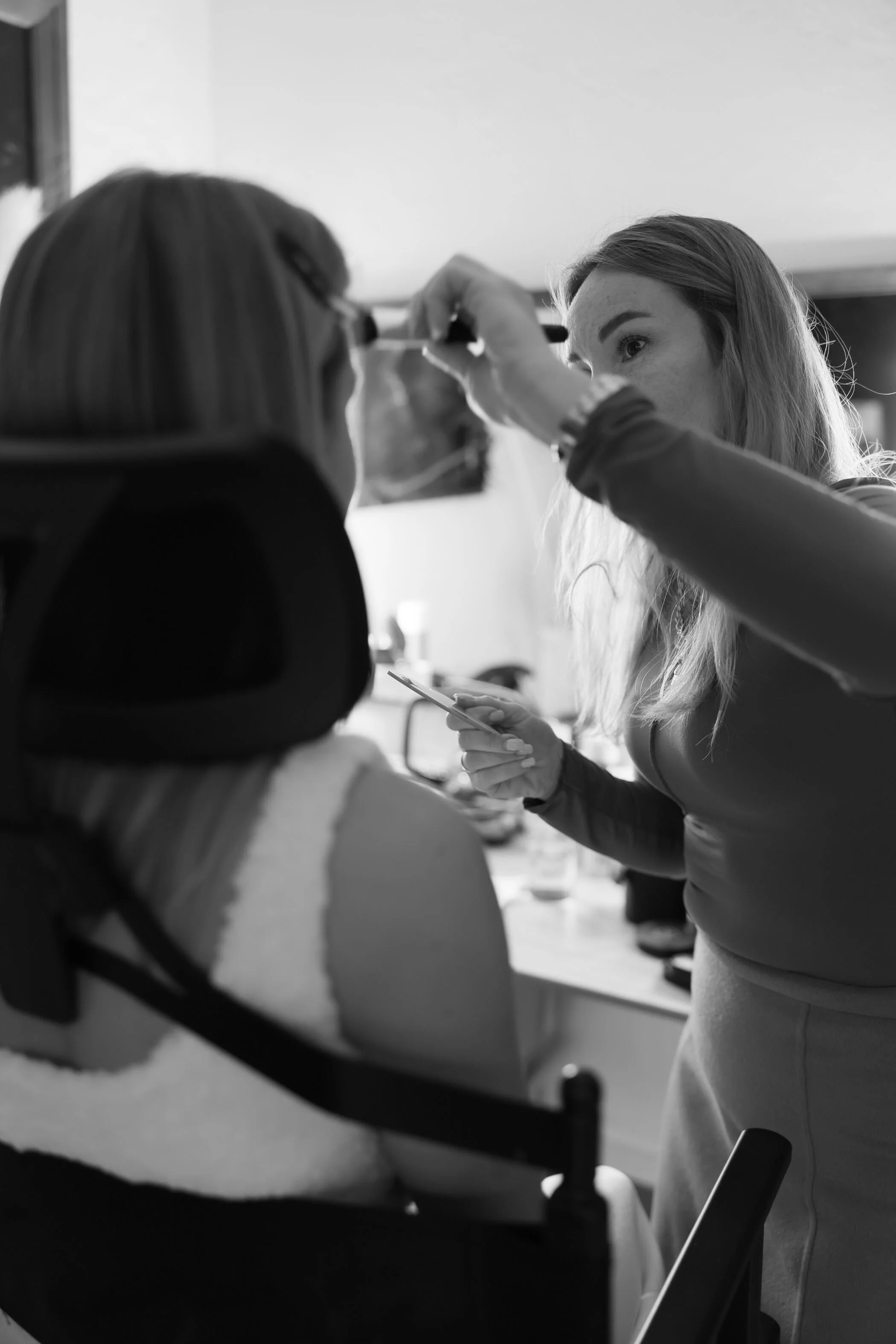 Makeup artist applying makeup on a woman with long hair in a salon or makeup studio.