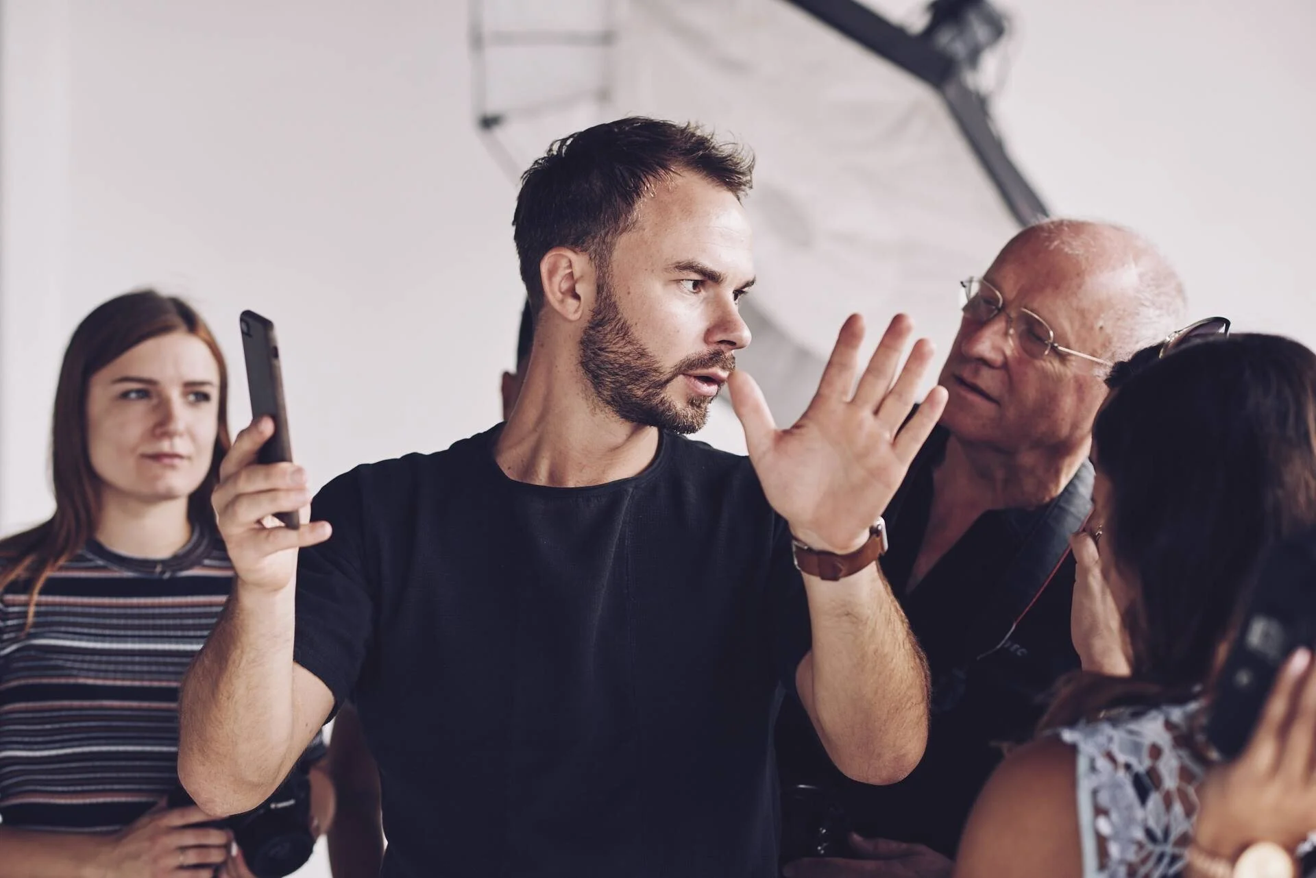 Man_gesturing_with_phone_in_photography_studio_with_onlookers.jpg