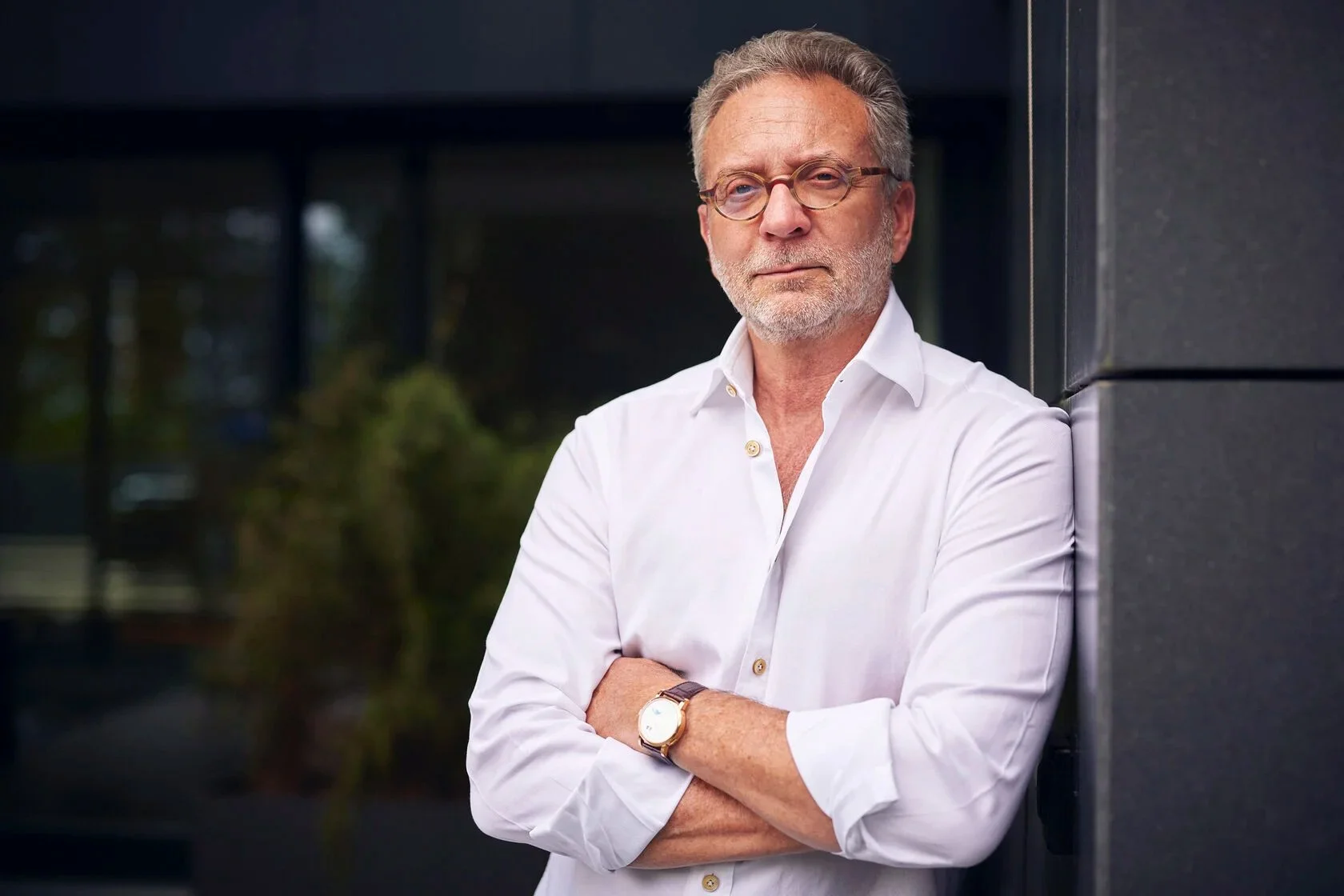 Man_in_White_Shirt_with_Arms_Crossed_Against_Dark_Wall.jpg