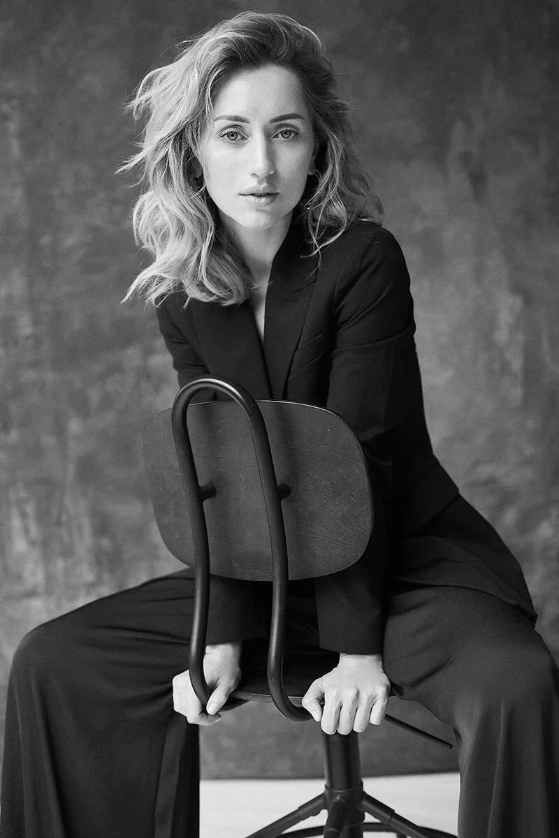 Woman_in_black_suit_seated_on_chair_with_hands_clasped.jpg