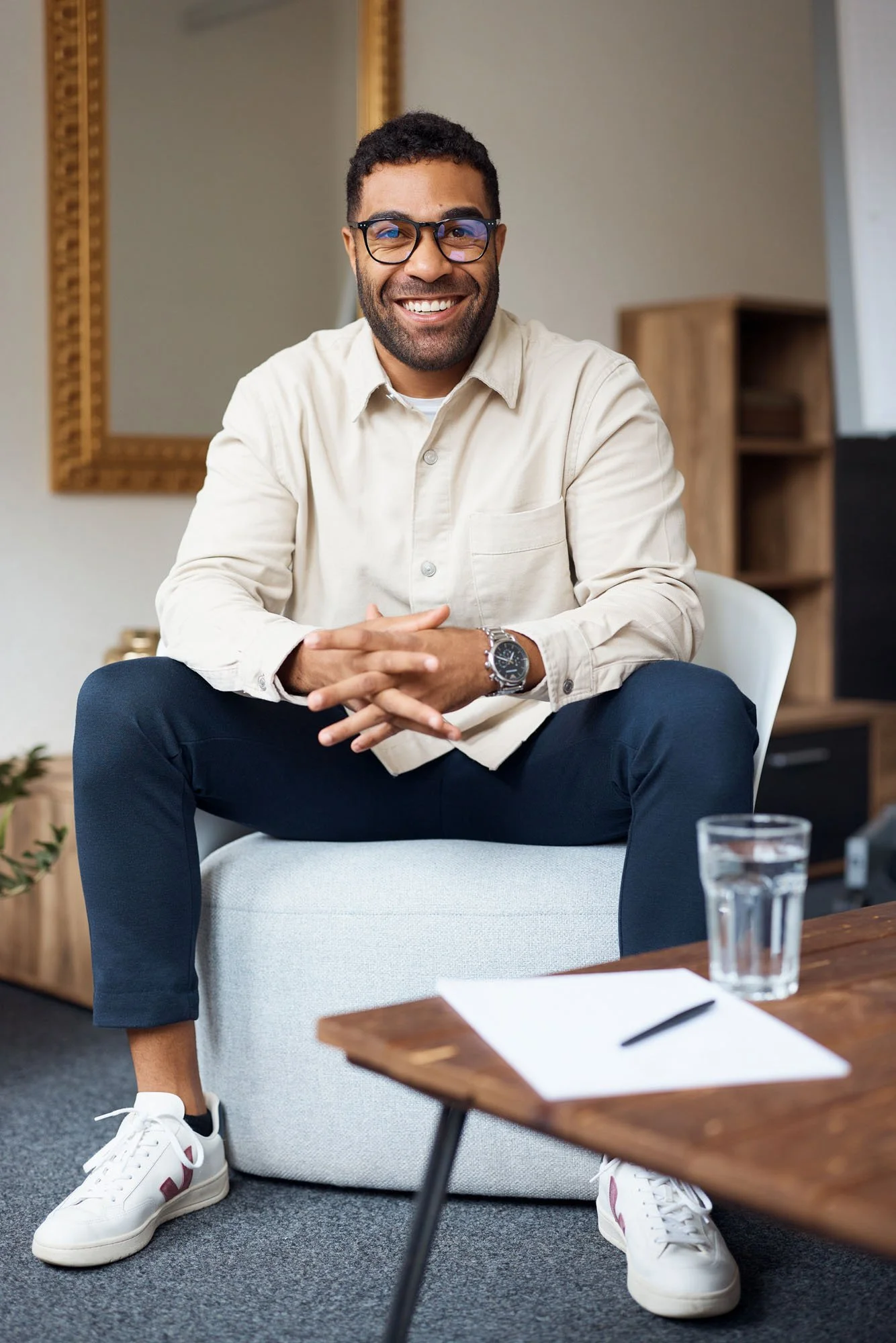Smiling_man_in_beige_shirt_and_glasses_sitting_indoors.jpeg
