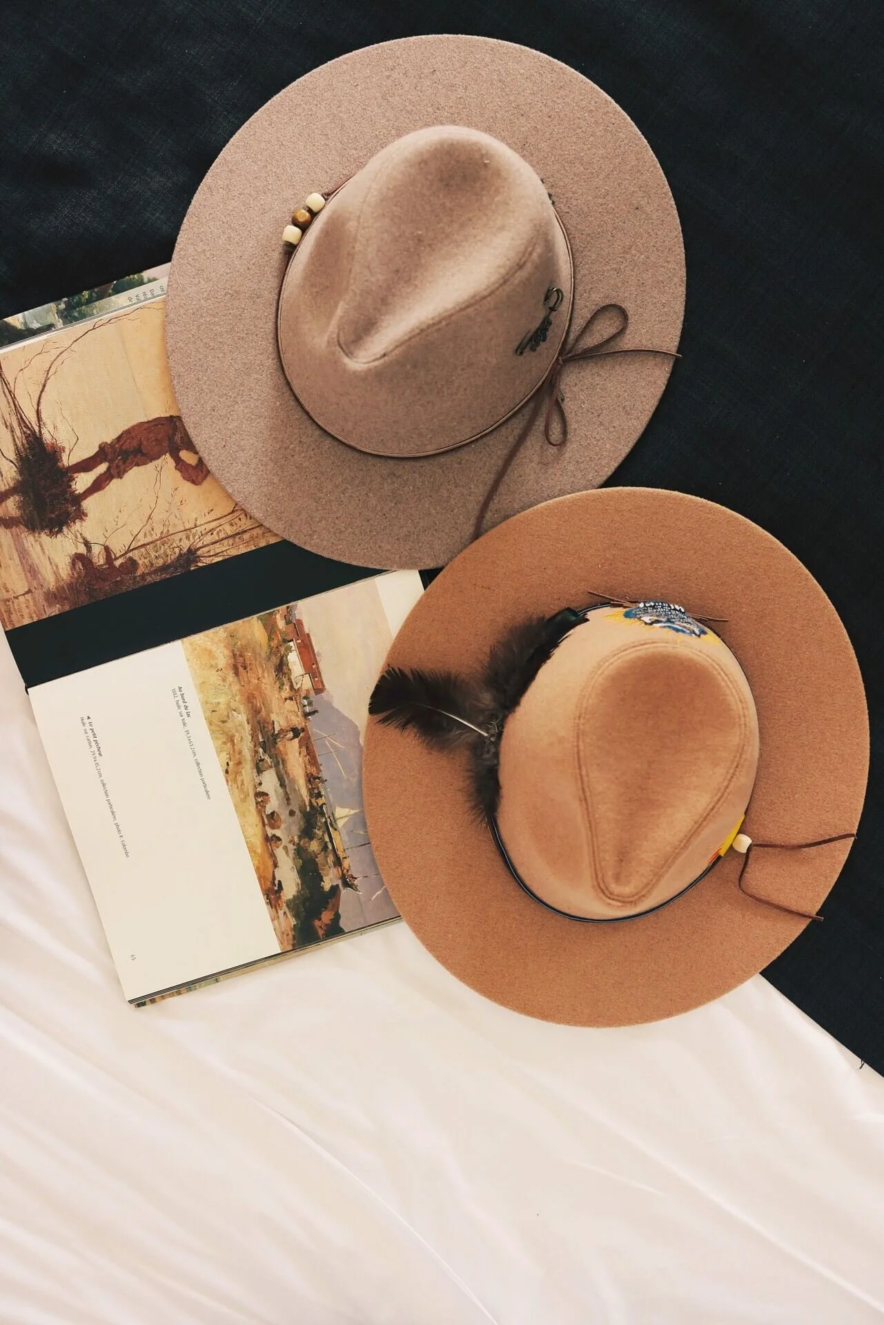 L'image représente deux chapeaux posés sur un livre ouvert avec des illustrations artistiques, sur un fond sombre. Capturée à Lausanne par un photographe portraitiste professionnel.