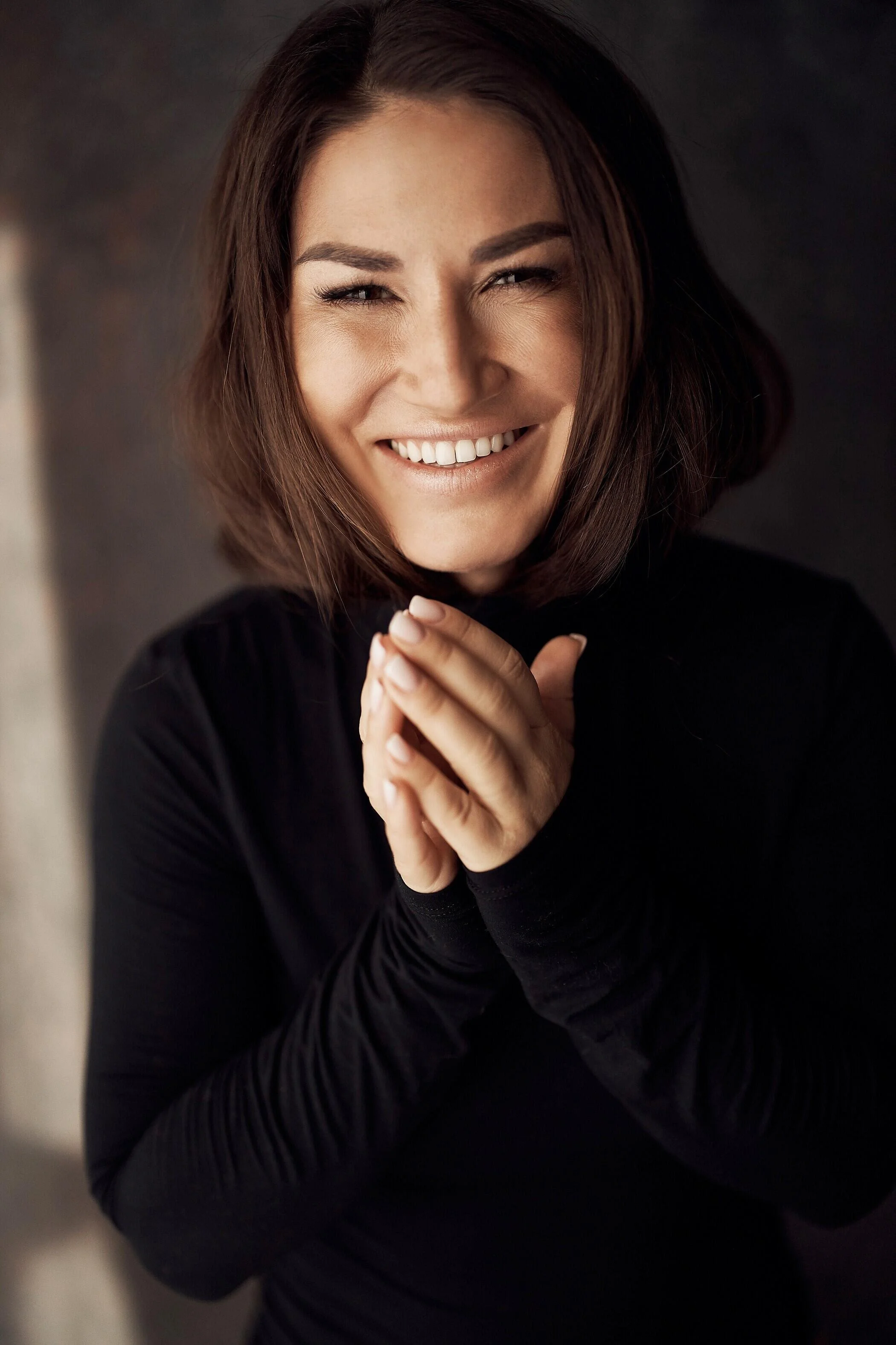 Smiling_woman_in_black_turtleneck_with_clasped_hands.jpg