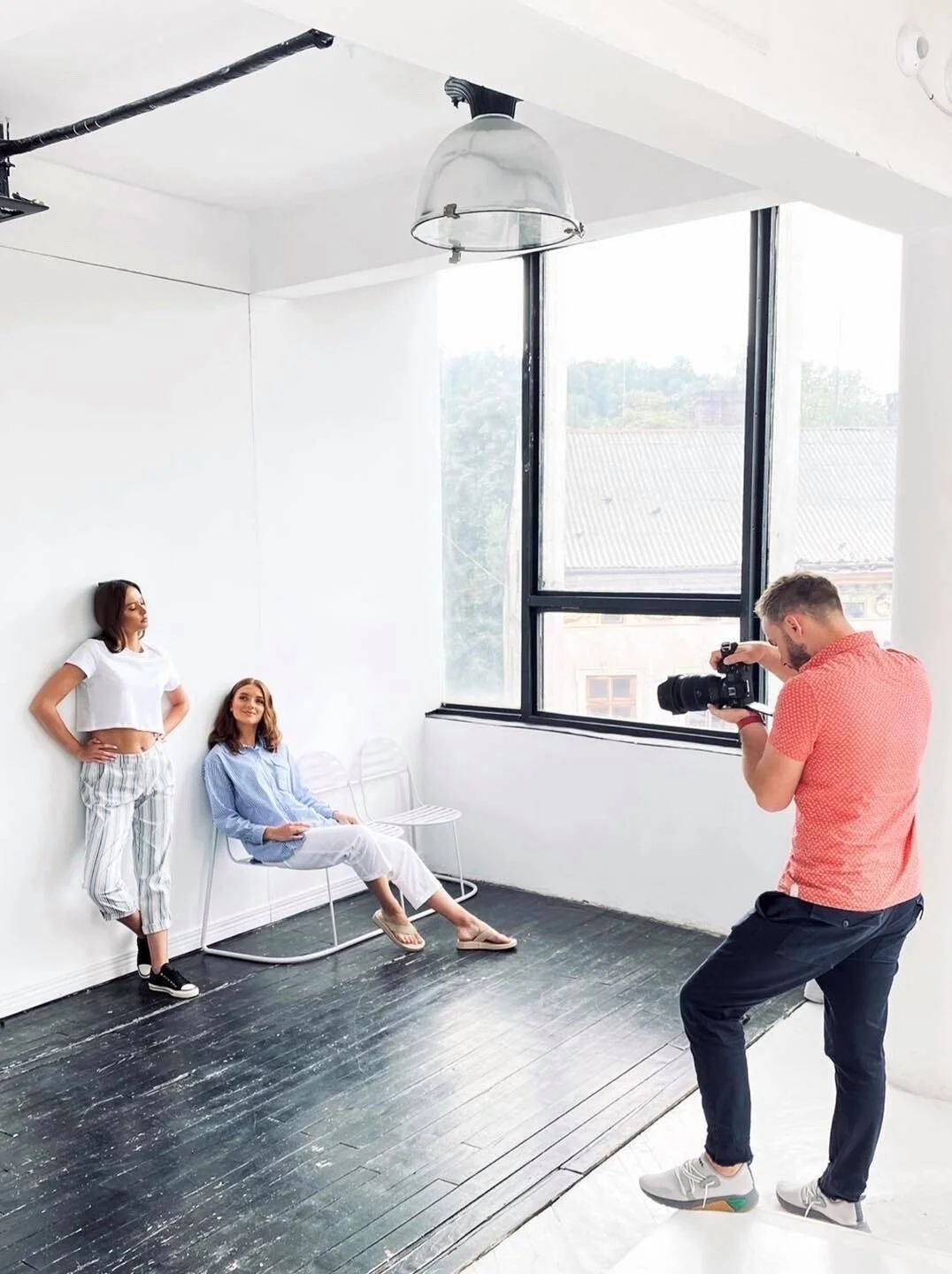 Le photographe prend des photos de deux femmes dans un studio lumineux et minimaliste avec de grandes fenêtres et des planchers en bois.