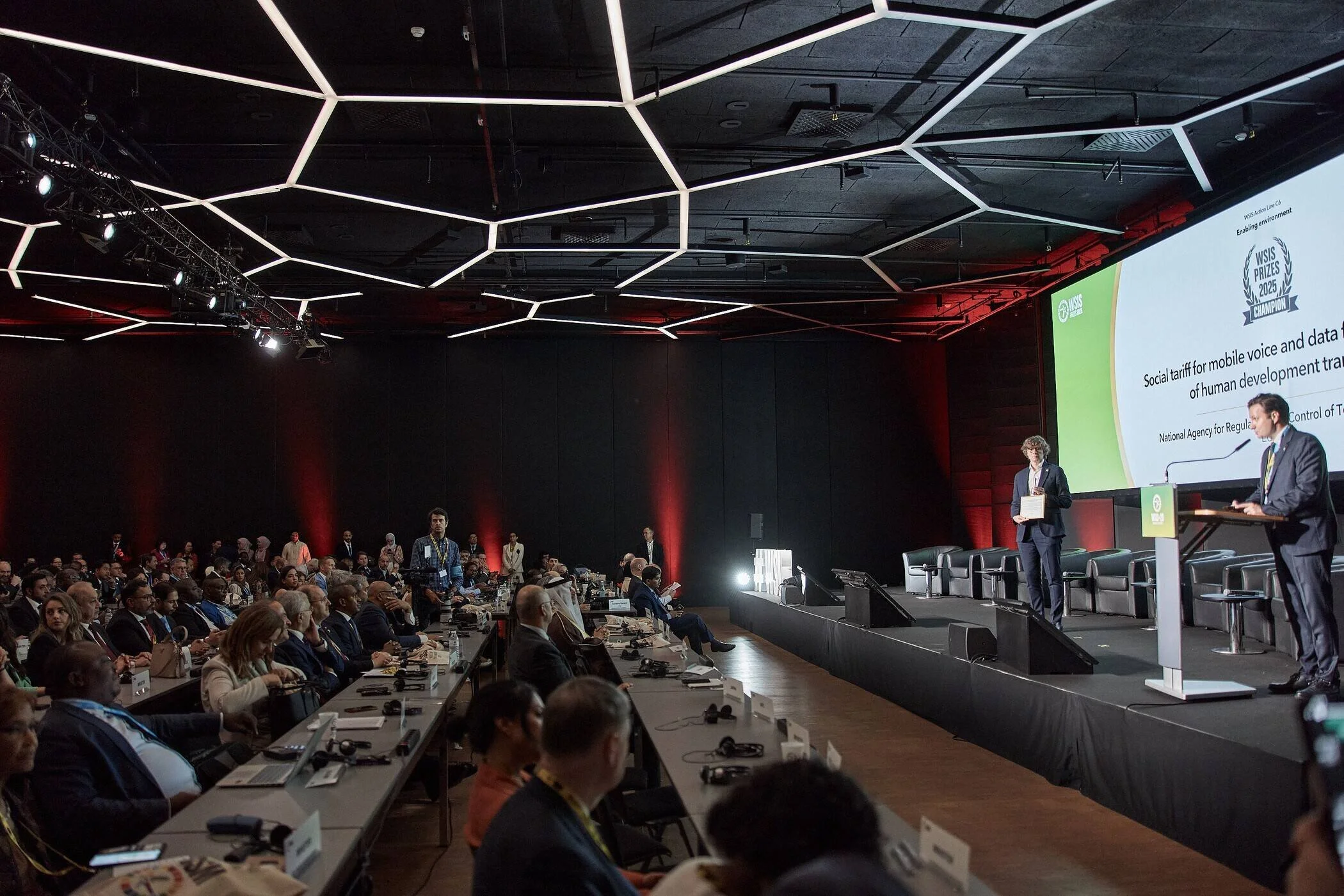 Conference_setting_with_audience_and_speakers_in_dark_room.jpg