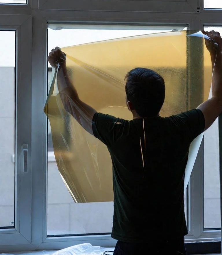 A person applying a large yellow film to a window.