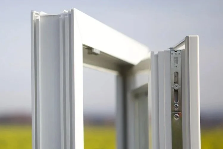 Close-up of a white window frame with visible metal hardware, set against a blurred outdoor background.