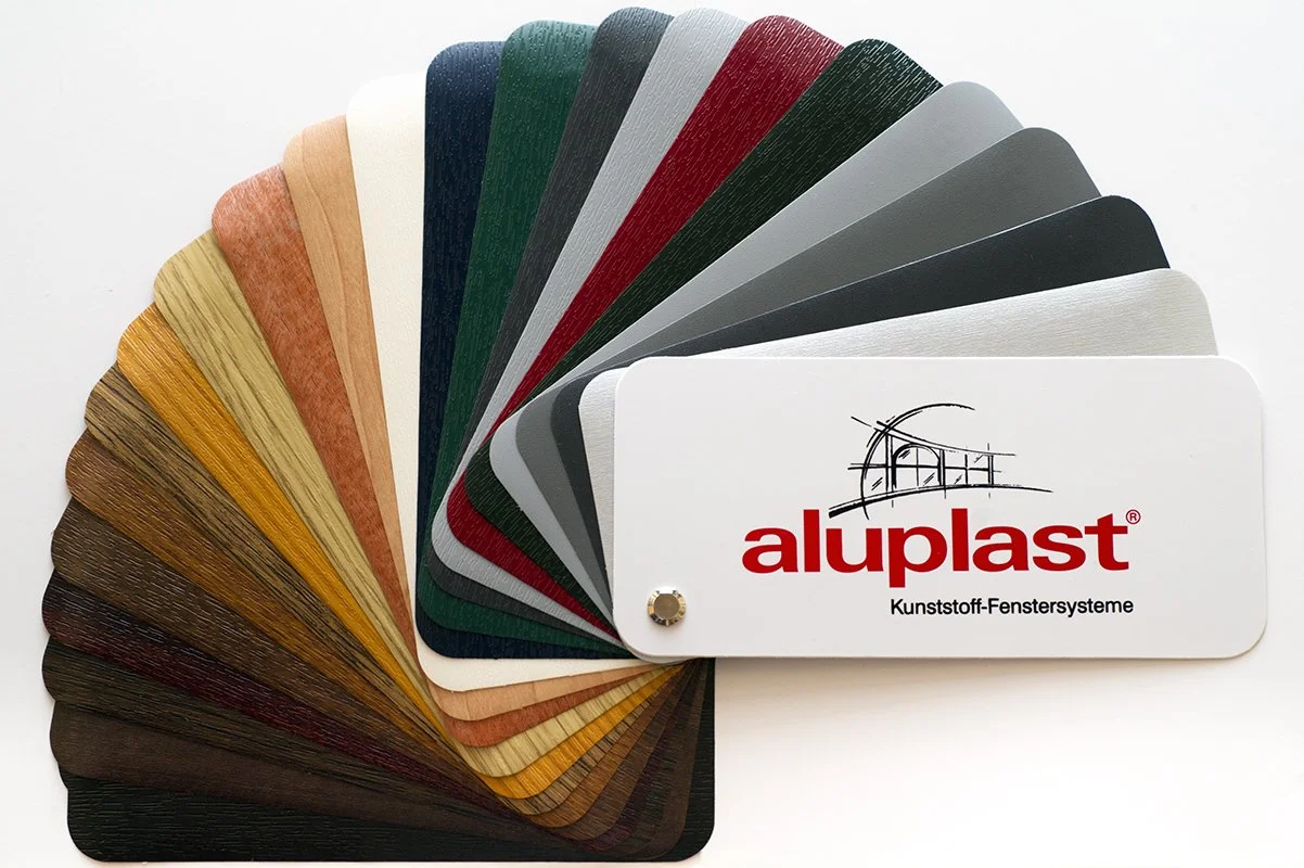 Color sample card with various colored laminate sheets fanned out, with a white sample card with 'aluplast' branding and logo.